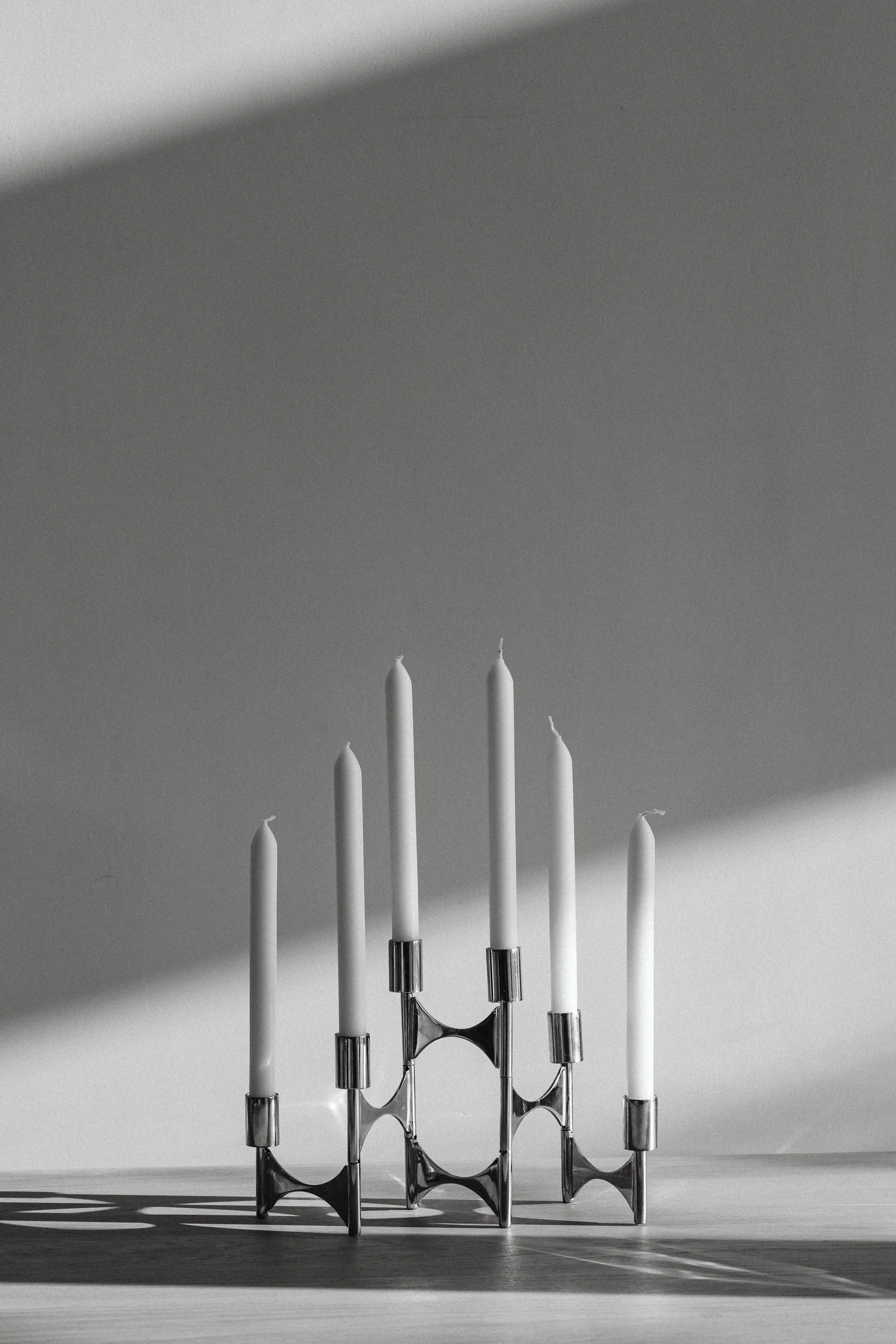 A black and white photograph of a chromed candelabrum with eight tall white candles, casting shadows on a flat surface.