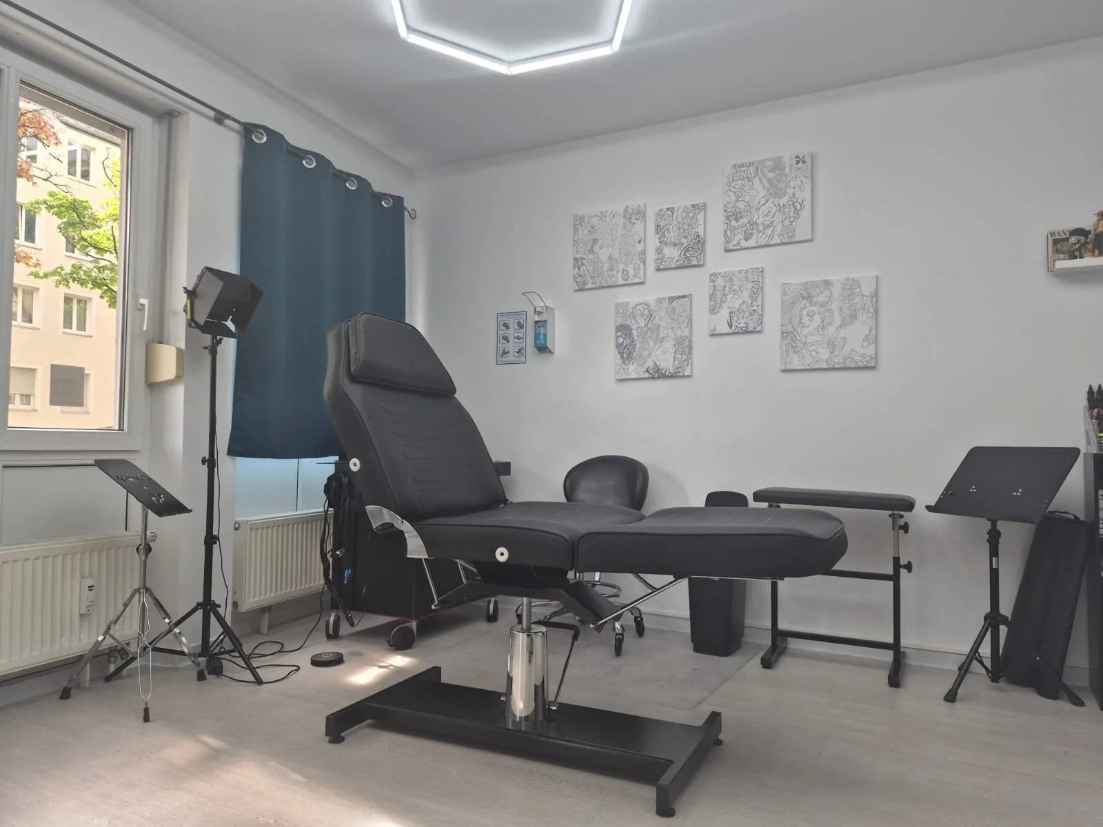 Behandlungsraum mit Untersuchungsliege, Stühlen, Lichtquellen, Kunstwerken an der Wand und Technikausstattung.