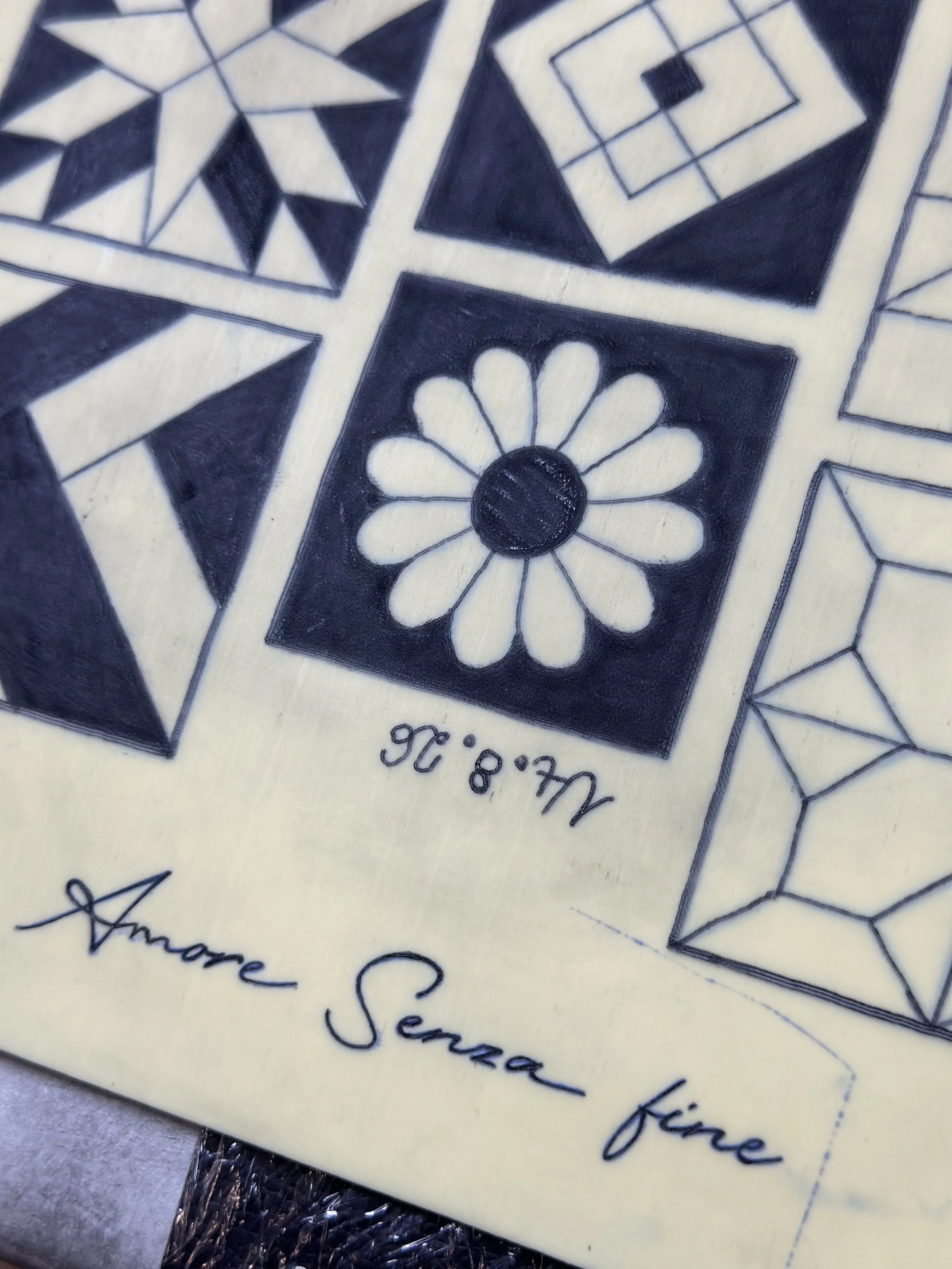 Nahaufnahme eines detailreichen schwarz-weißen geometrischen Musters auf einer Oberflächentafel, mit Schriftzug darunter.
