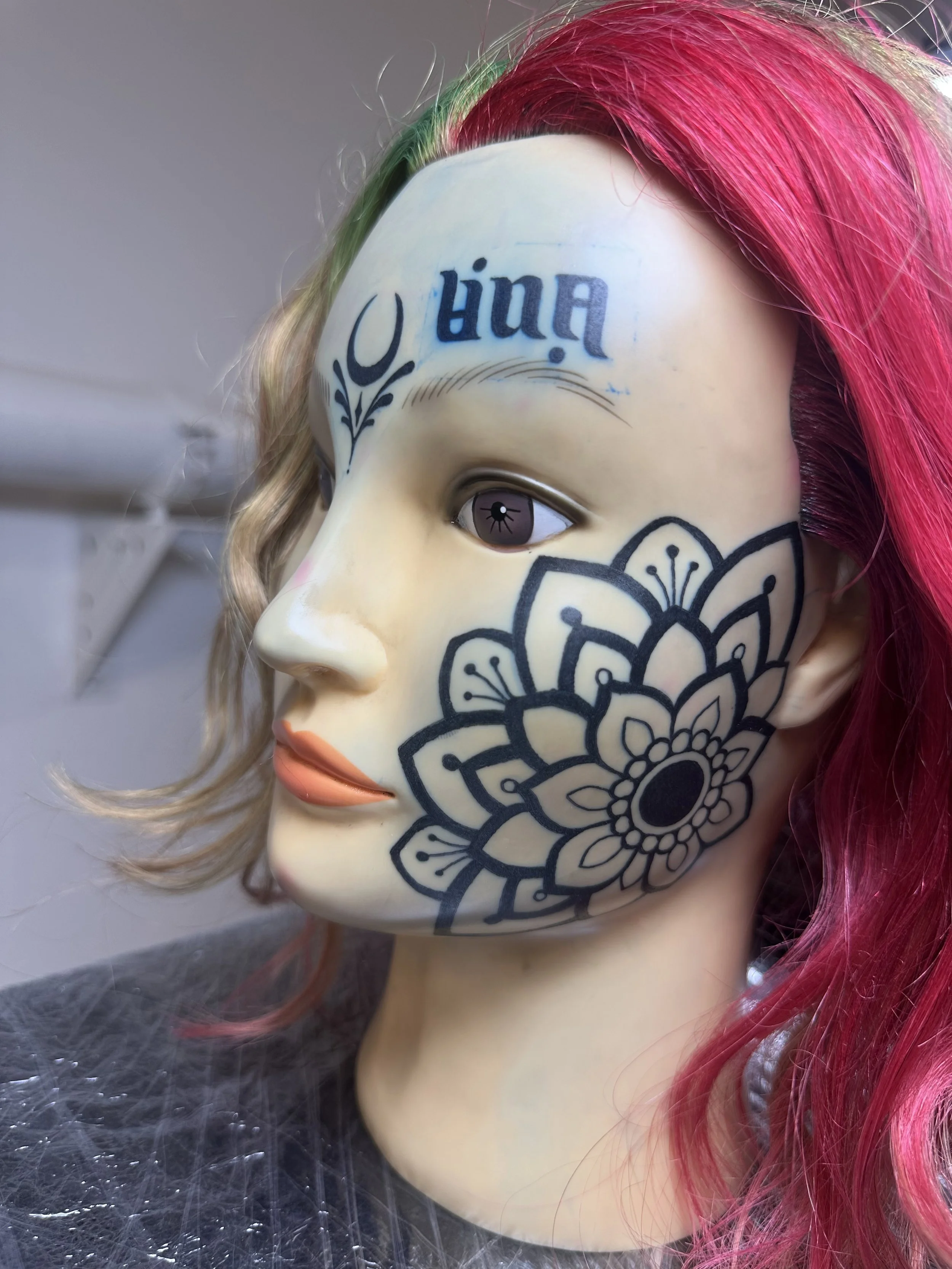 Eine Maske mit einem femininen Gesicht, markierter Stirn mit Tattoo, pinken Haaren und einem schwarzen Innenteil.