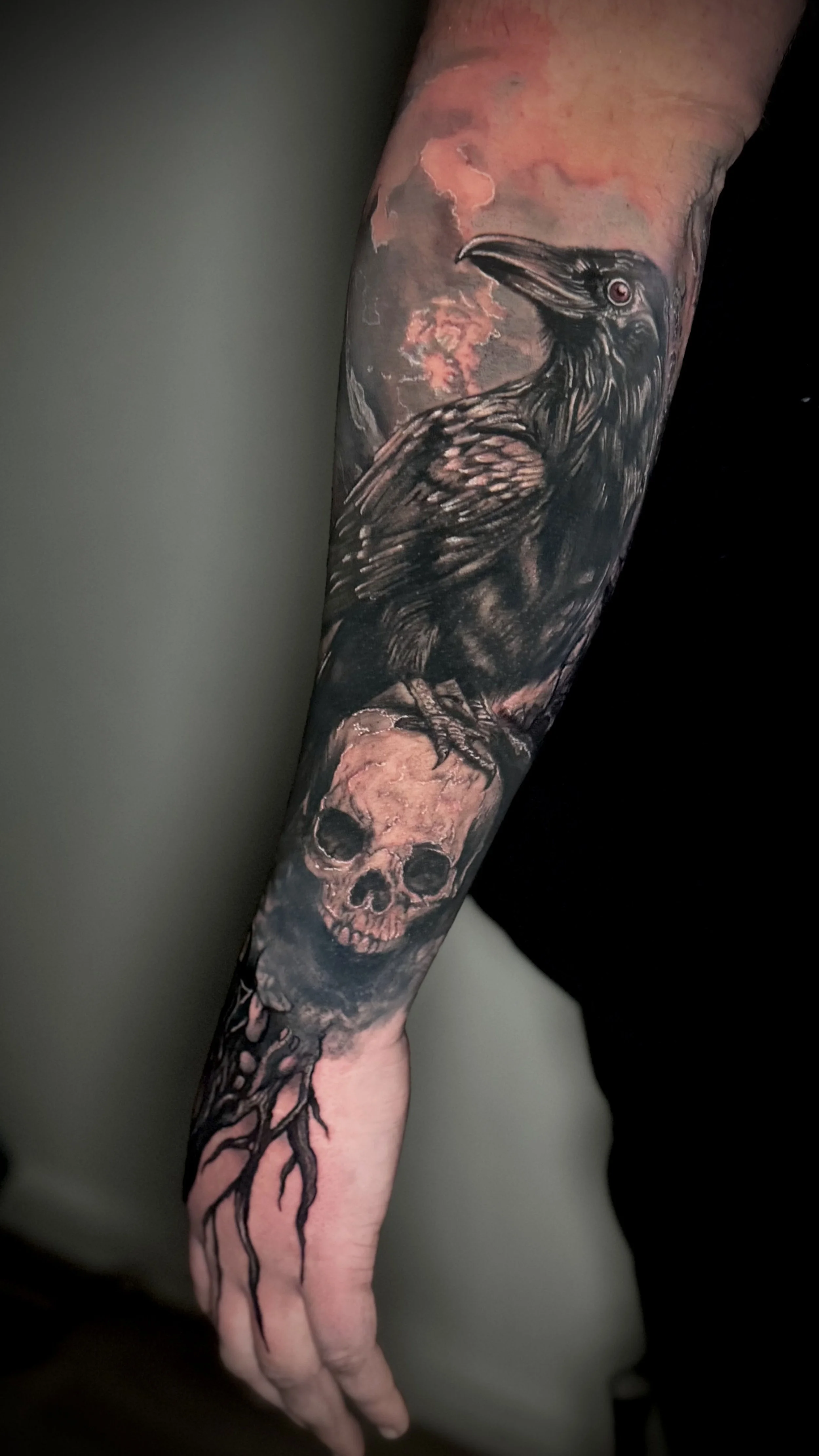 Ein Arm-Tattoo mit einem schwarz-weißen Raben, der auf einem Baum sitzt, und einem Totenschädel darunter.