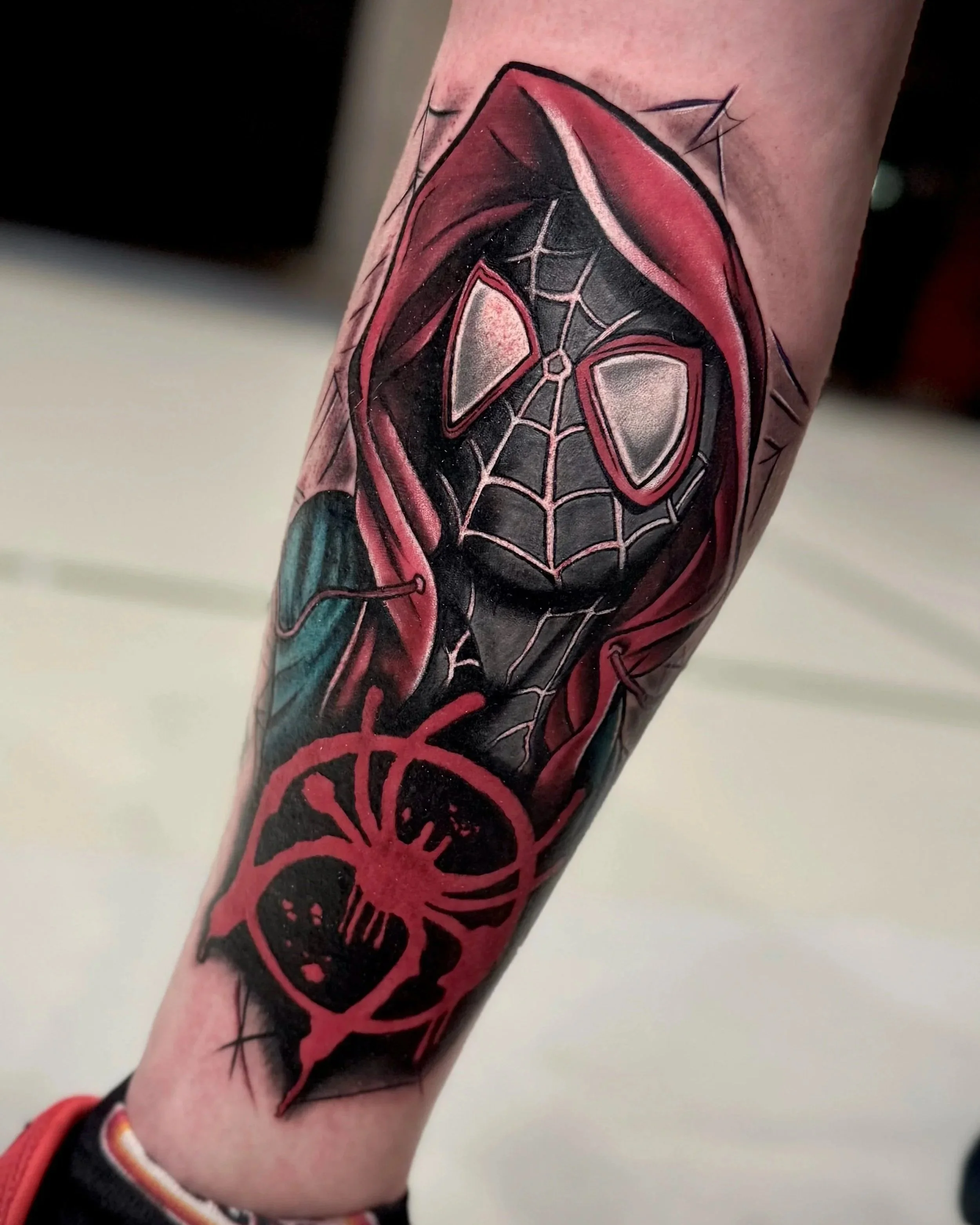 Tattoo eines schwarzen und roten Spinnennetzes mit einer Spinne am Unterarm.