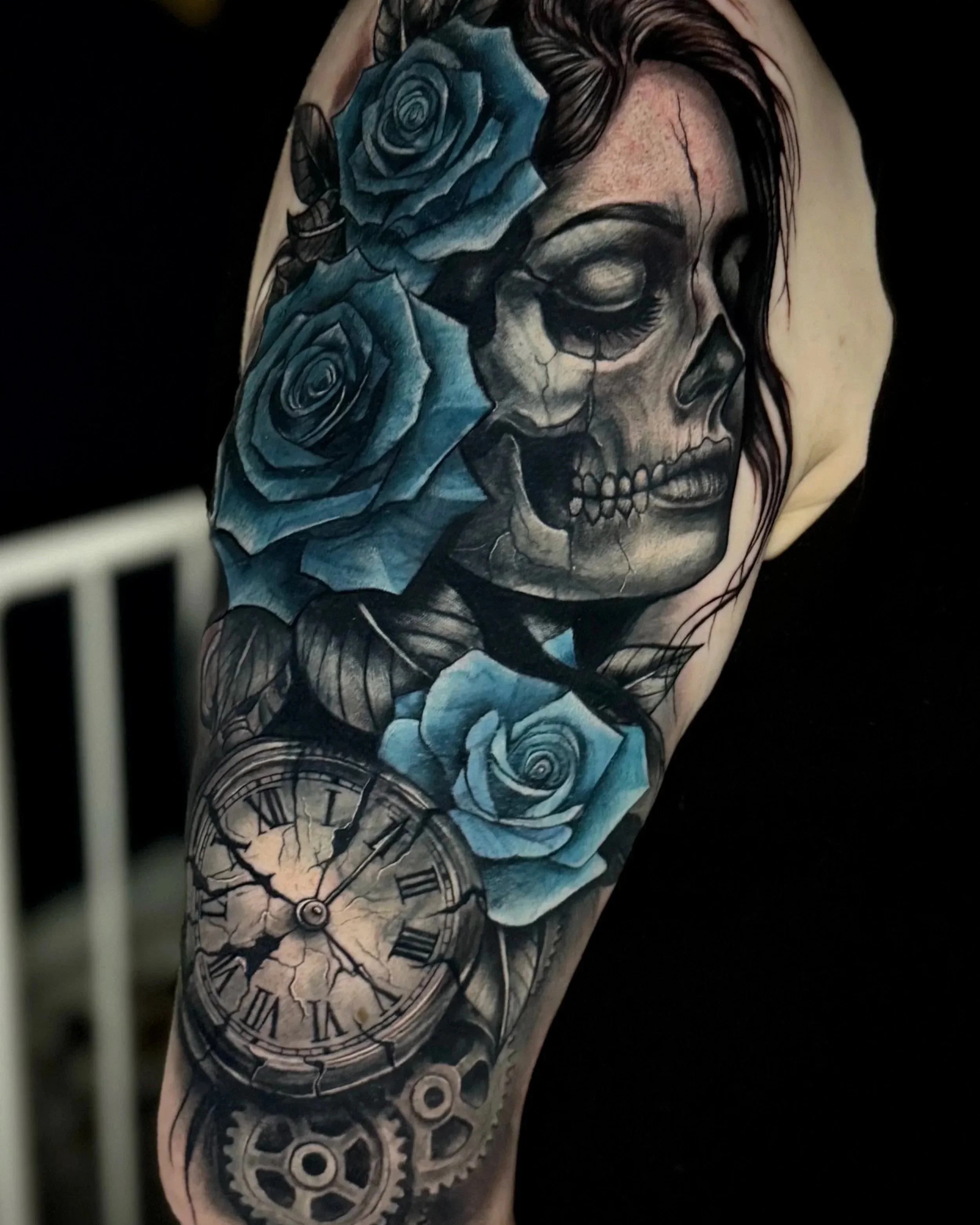 Tattoo auf einem Arm, das eine chemische Uhr, blaue Rosen und ein Skelett enthält.