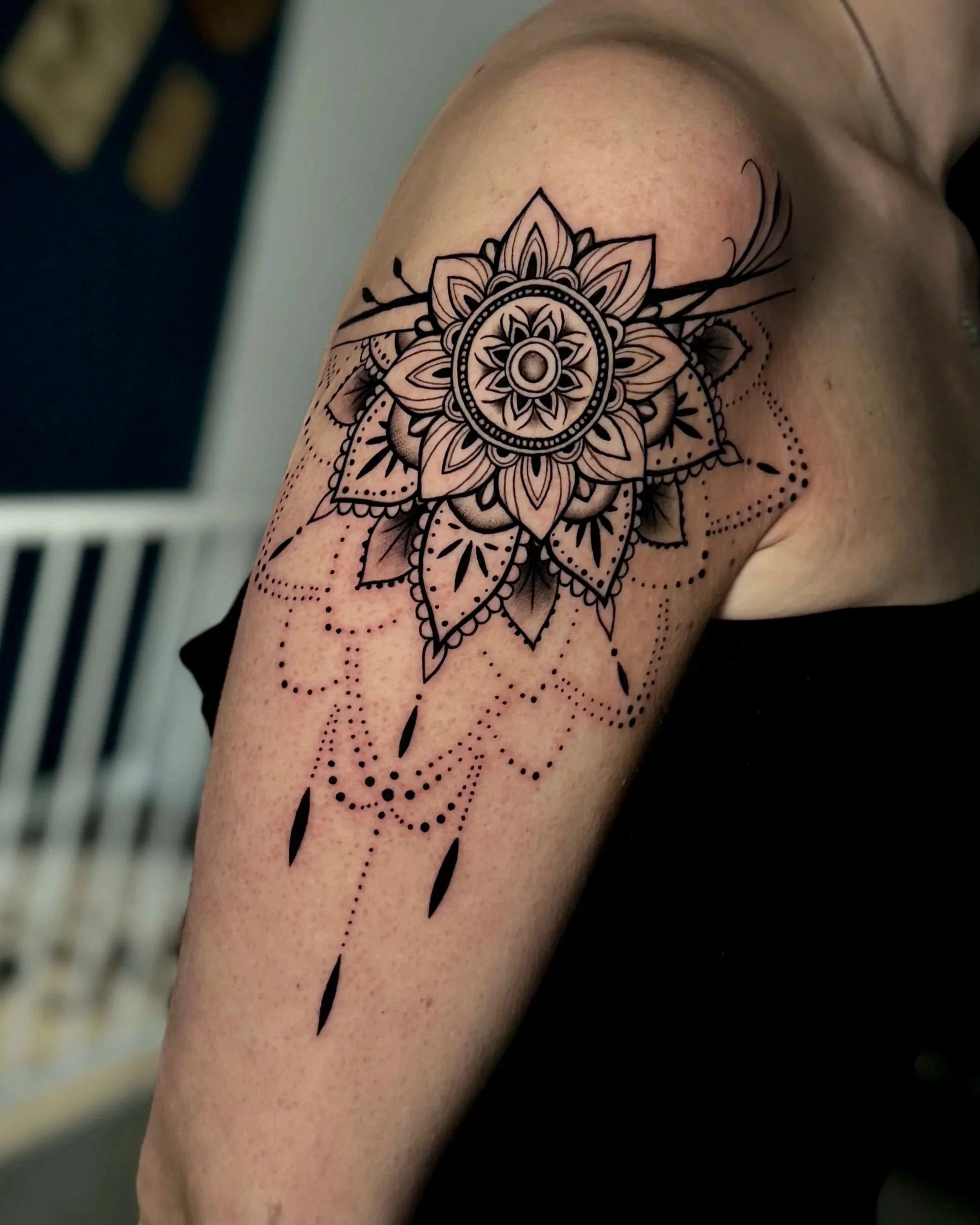 Eine Tätowierung in Mandala-Design auf dem Oberarm mit schwarzen Linien und detailreichen Mustern.
