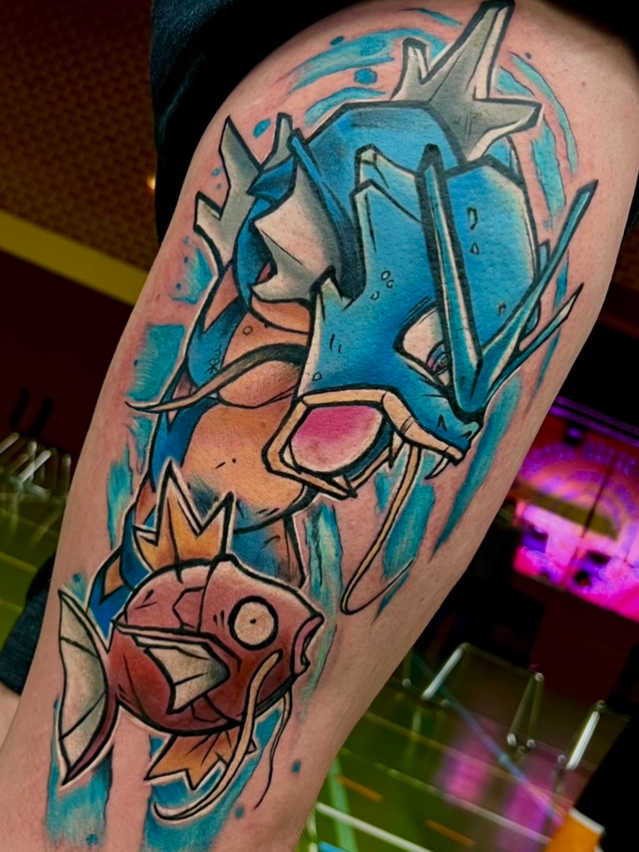Farbige Pokémon-Tätowierung von Garados und Karpador im Anime-Stil auf dem Oberschenkel. 