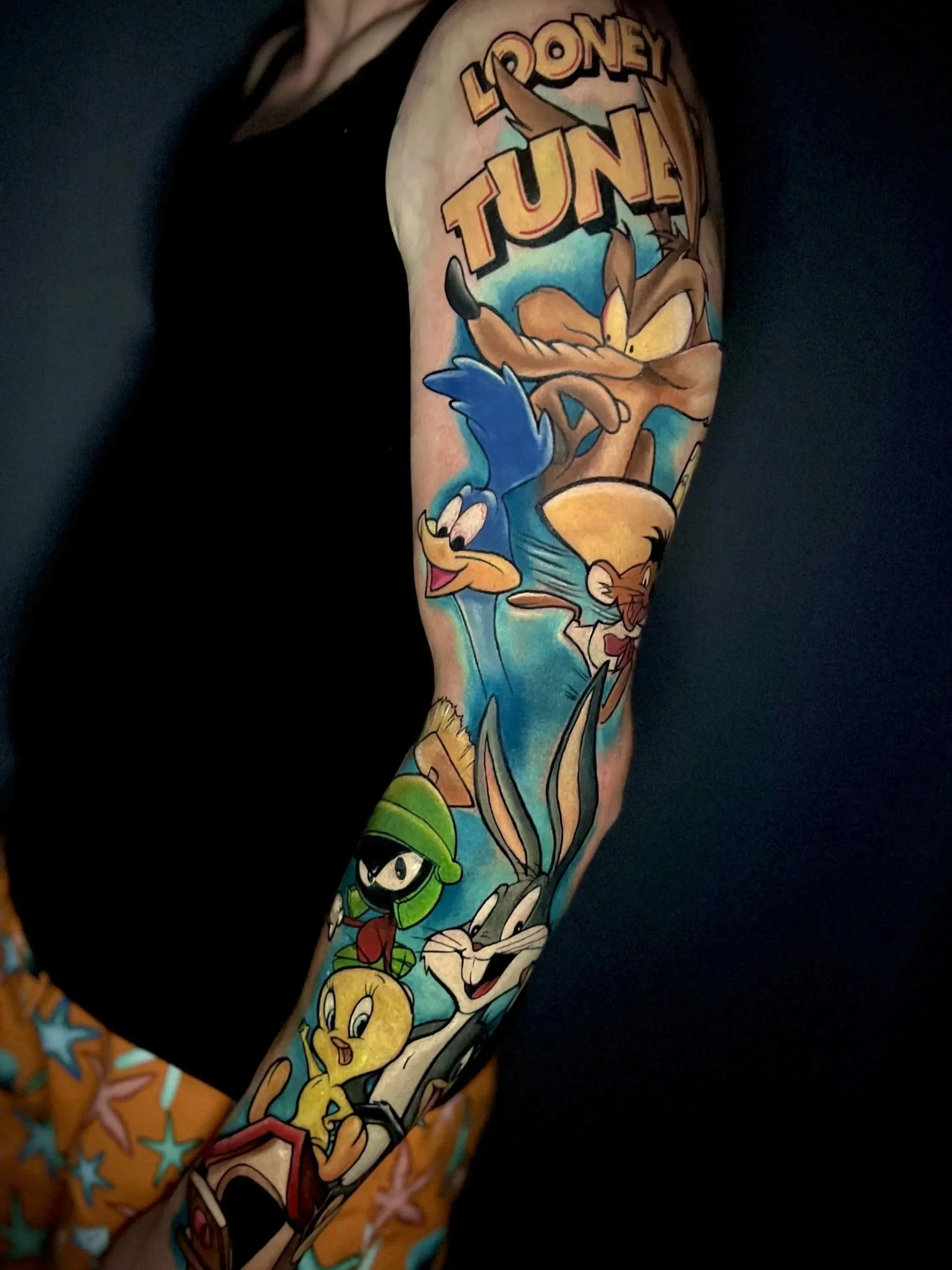 Farbige Looney Tunes Tätowierung mit Bugs Bunny, Wile E. Coyote, Road Runner, Tweety und Marvin Martian als Comic-Sleeve am Arm. 