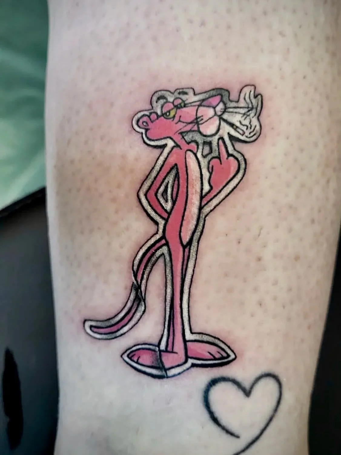 Tattoo eines Cartoon-Charakters, der eine Zigarette raucht, mit einem Herz daneben auf der Haut.
