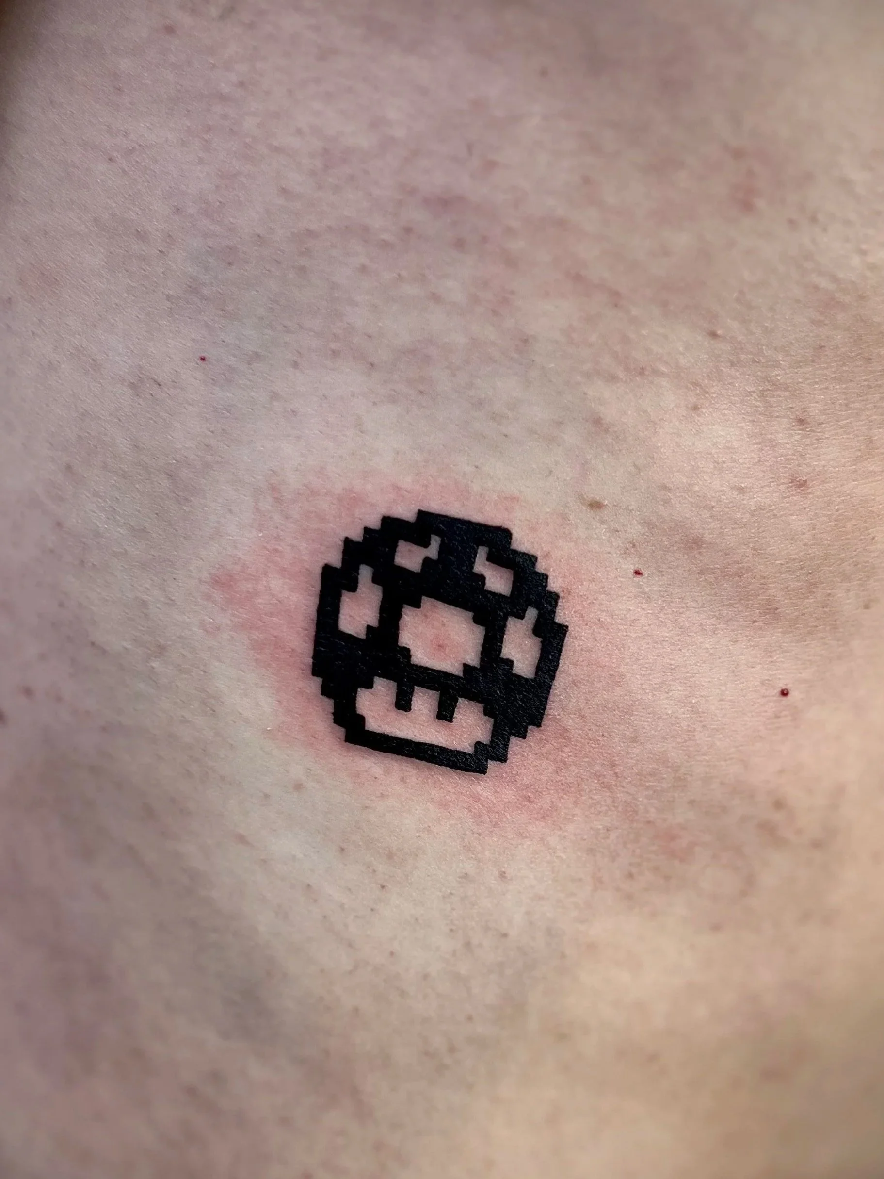 Näheaufnahme eines menschlichen Körpers mit einem schwarzen pixelartigen QR-Code-Tattoo auf der Haut.