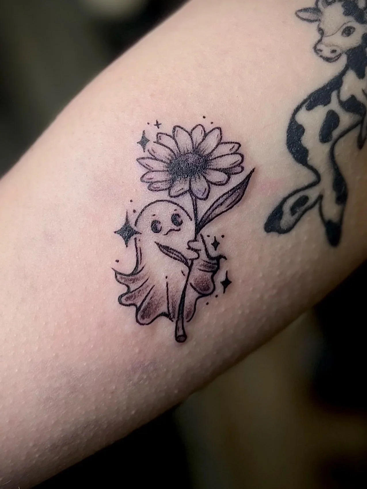 Tattoo eines fröhlichen Einhorns, das eine große Sonnenblume hält, mit kleinen funkelnden Sternen umgeben.