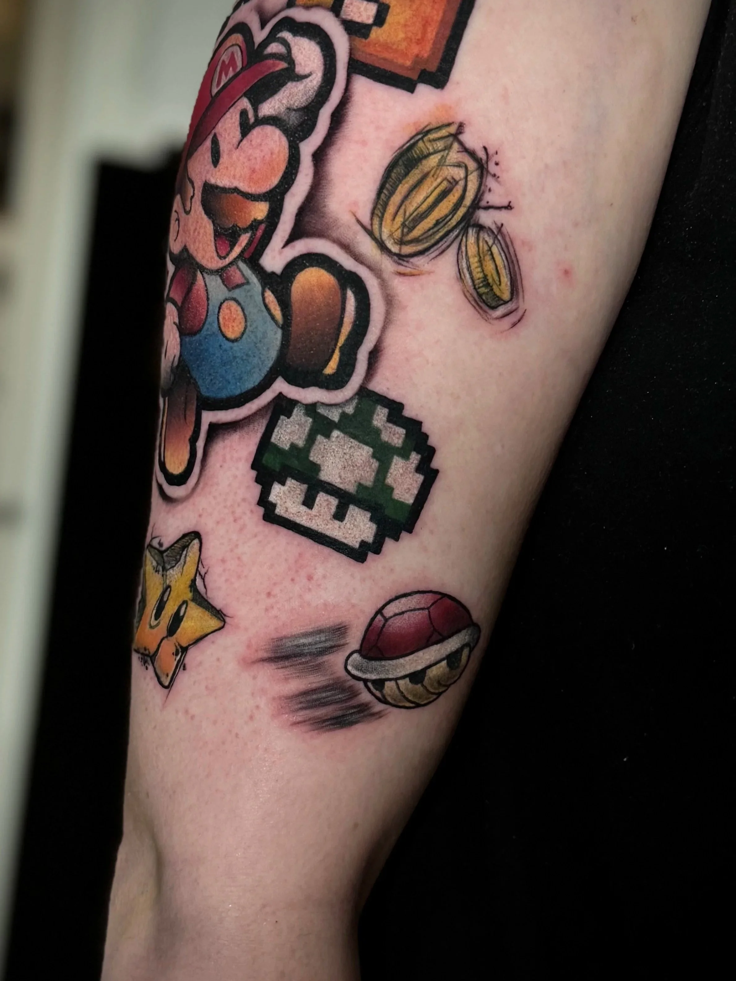 Tattoo eines Mario-Charakters, einer Münze, eines Pilzes, eines Koopa-Shells und eines Shy-Guy, inspiriert von Super Mario, auf dem Unterarm.