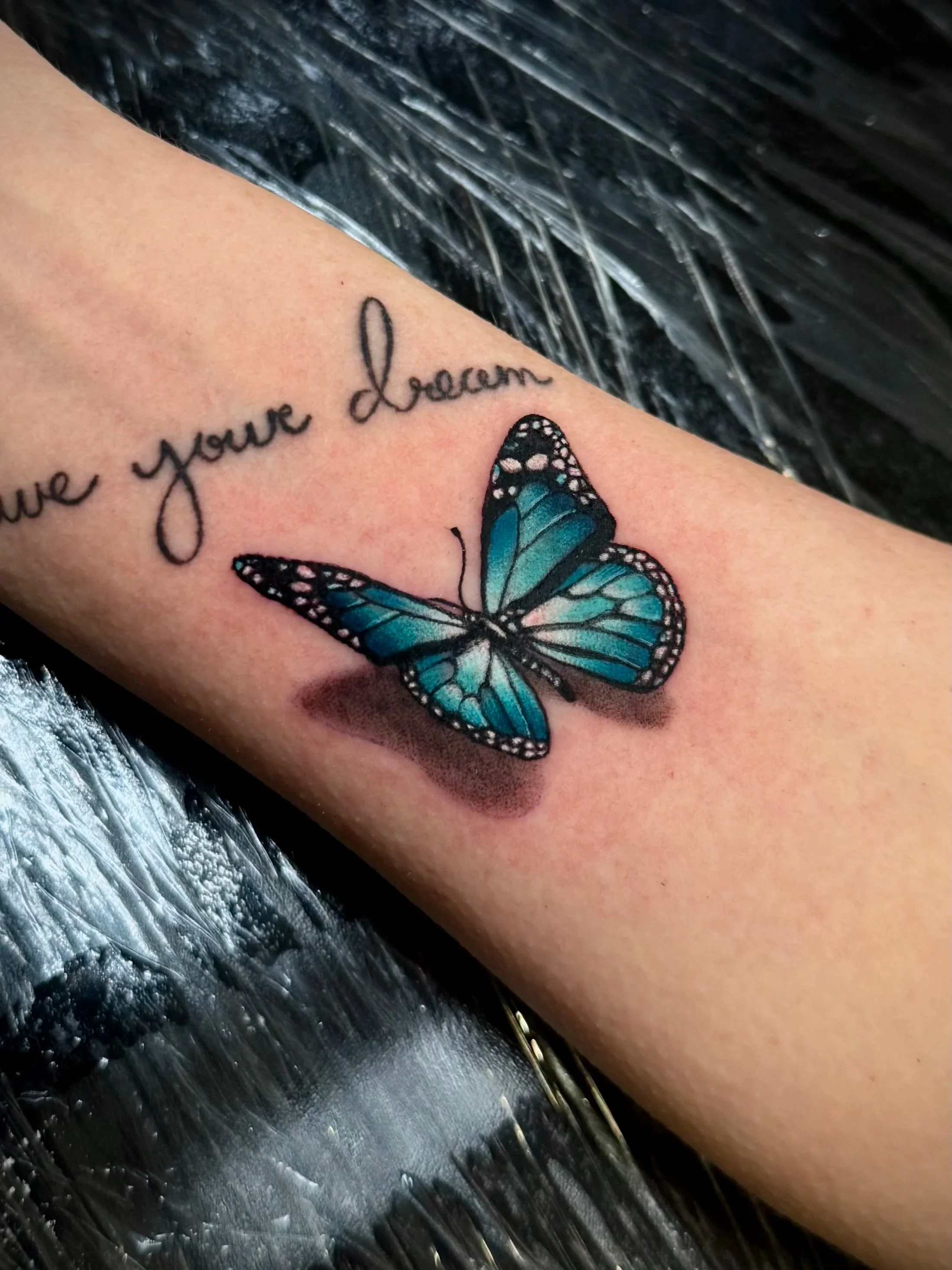 Tattoo auf einem Arm mit dem Text 'love your dream' und einem blauen Schmetterling.