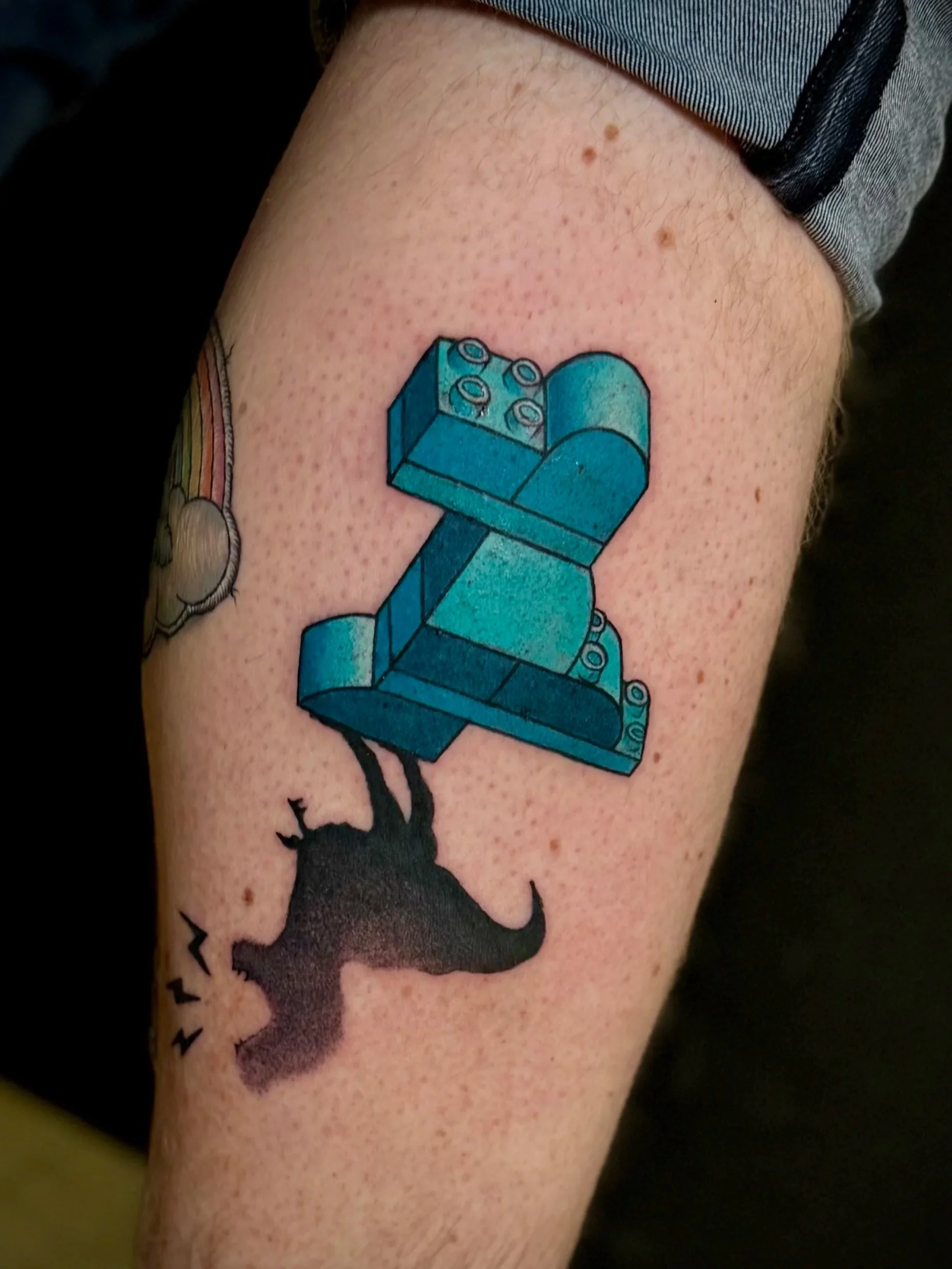 Tattoo eines Lego-Steins in blauer Farbe auf dem Oberarm
