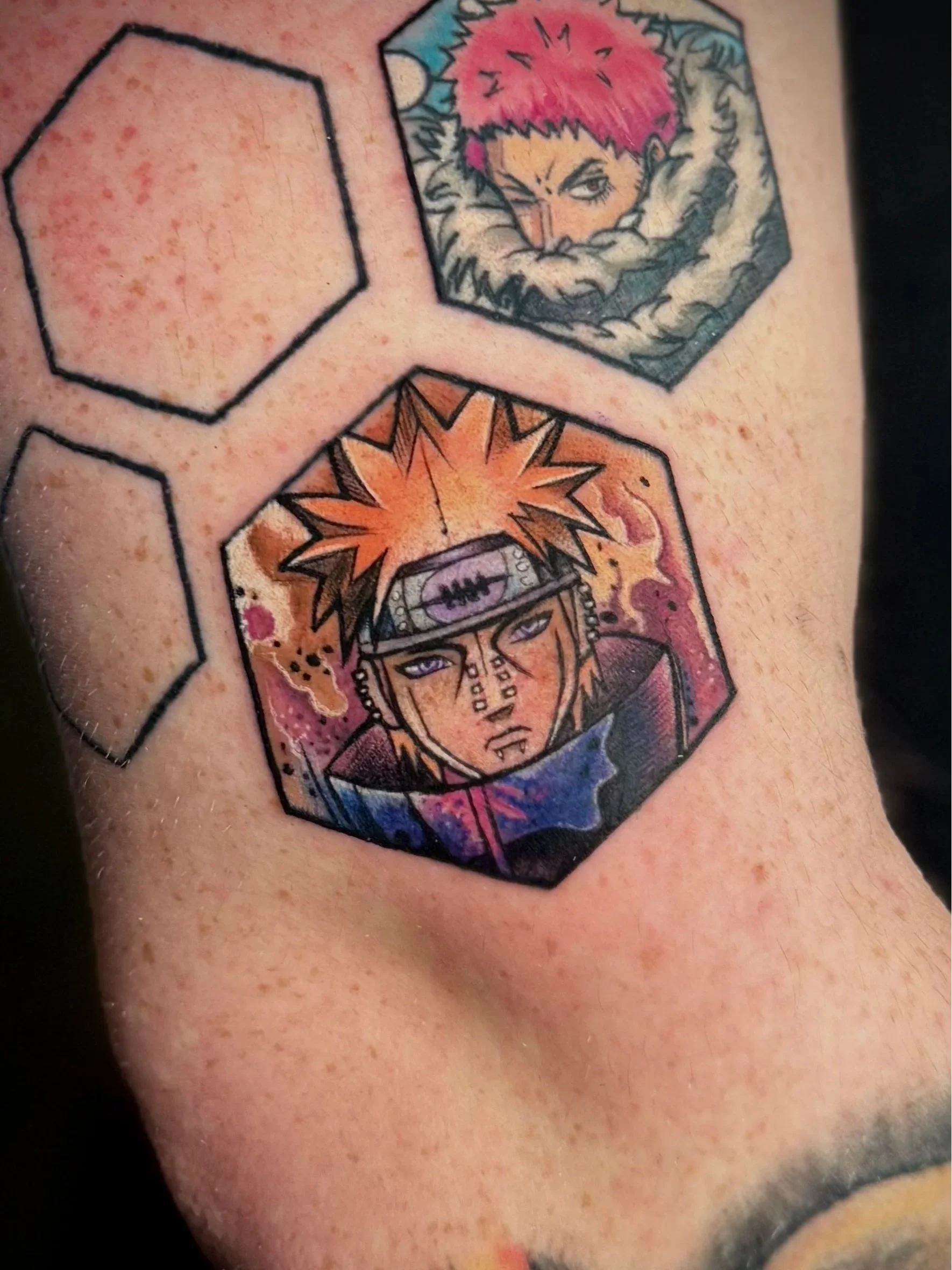 Tattoo auf der Haut, zeigt zwei Comic- oder Manga-Charaktere in Sepia- und Pink-Farben, in hexagonaler Form angeordnet.