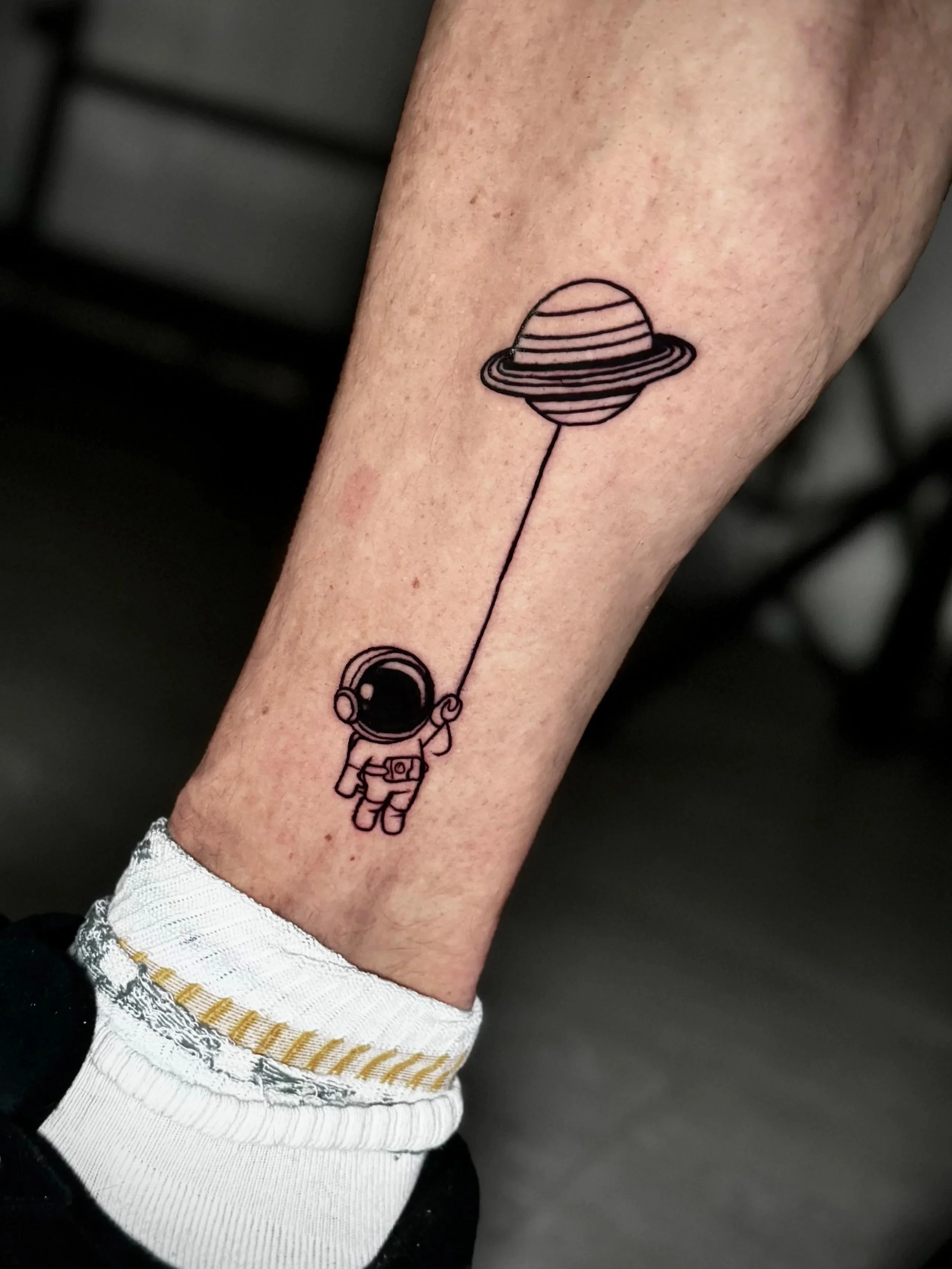 Tattoo eines Astronauten, der einen Ballon in Form eines Planeten mit Ringen hält.