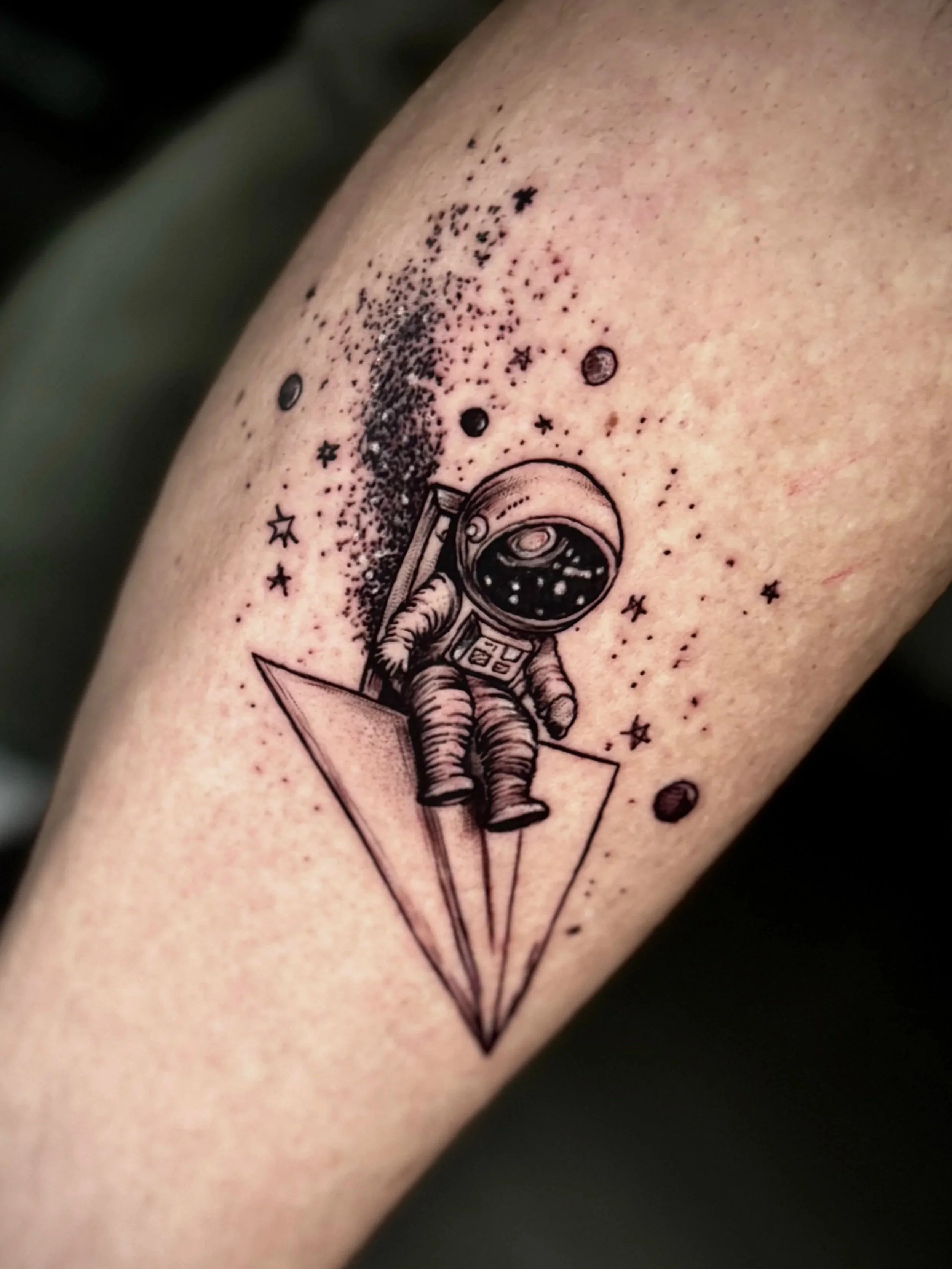 Tattoo eines Astronauten, der auf eine Rakete steht, im Weltraum mit Sternen und Planeten im Hintergrund.