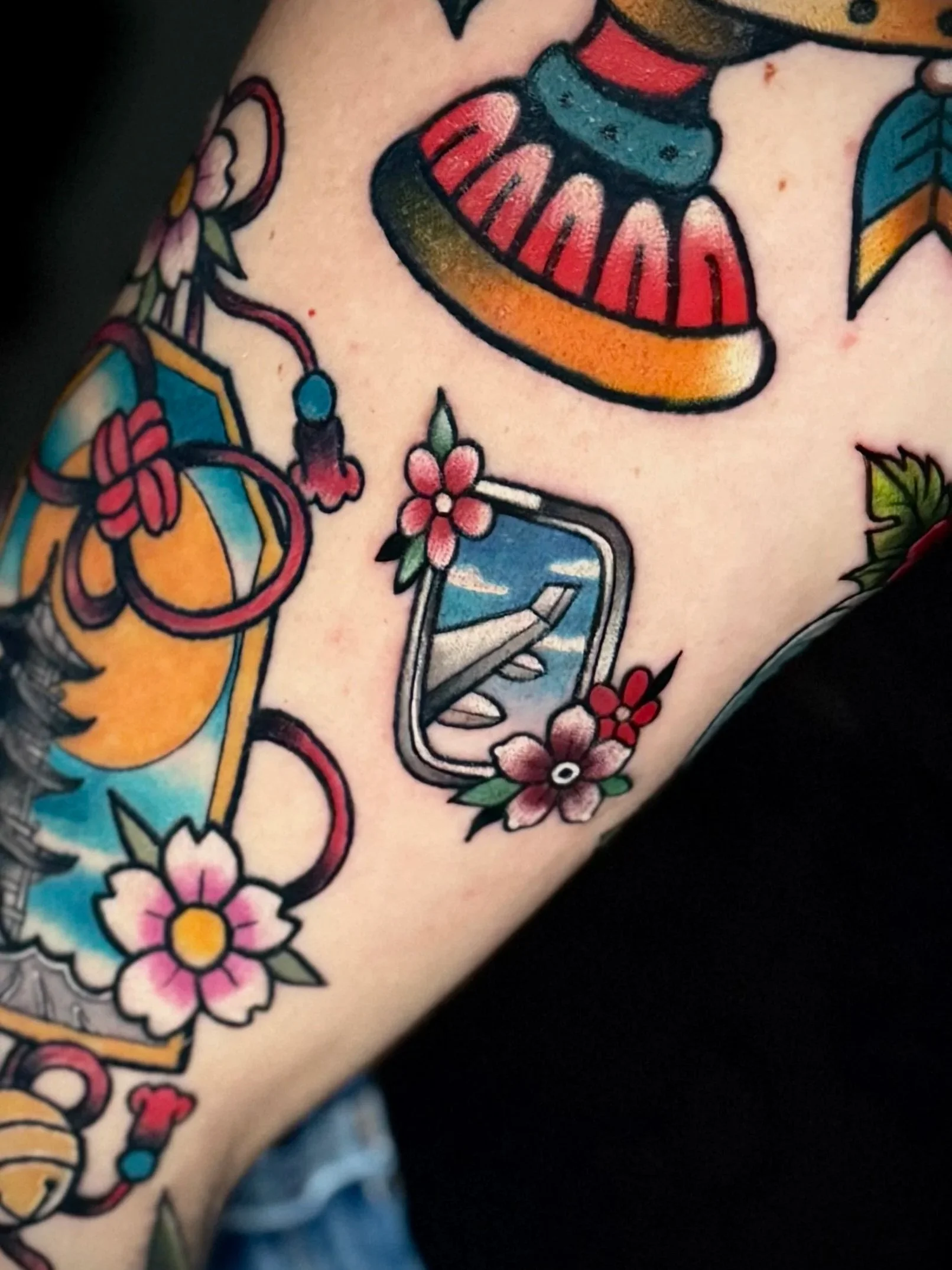 Tattoo mit Blumen, einer Flasche und einem Telefon auf der Haut.