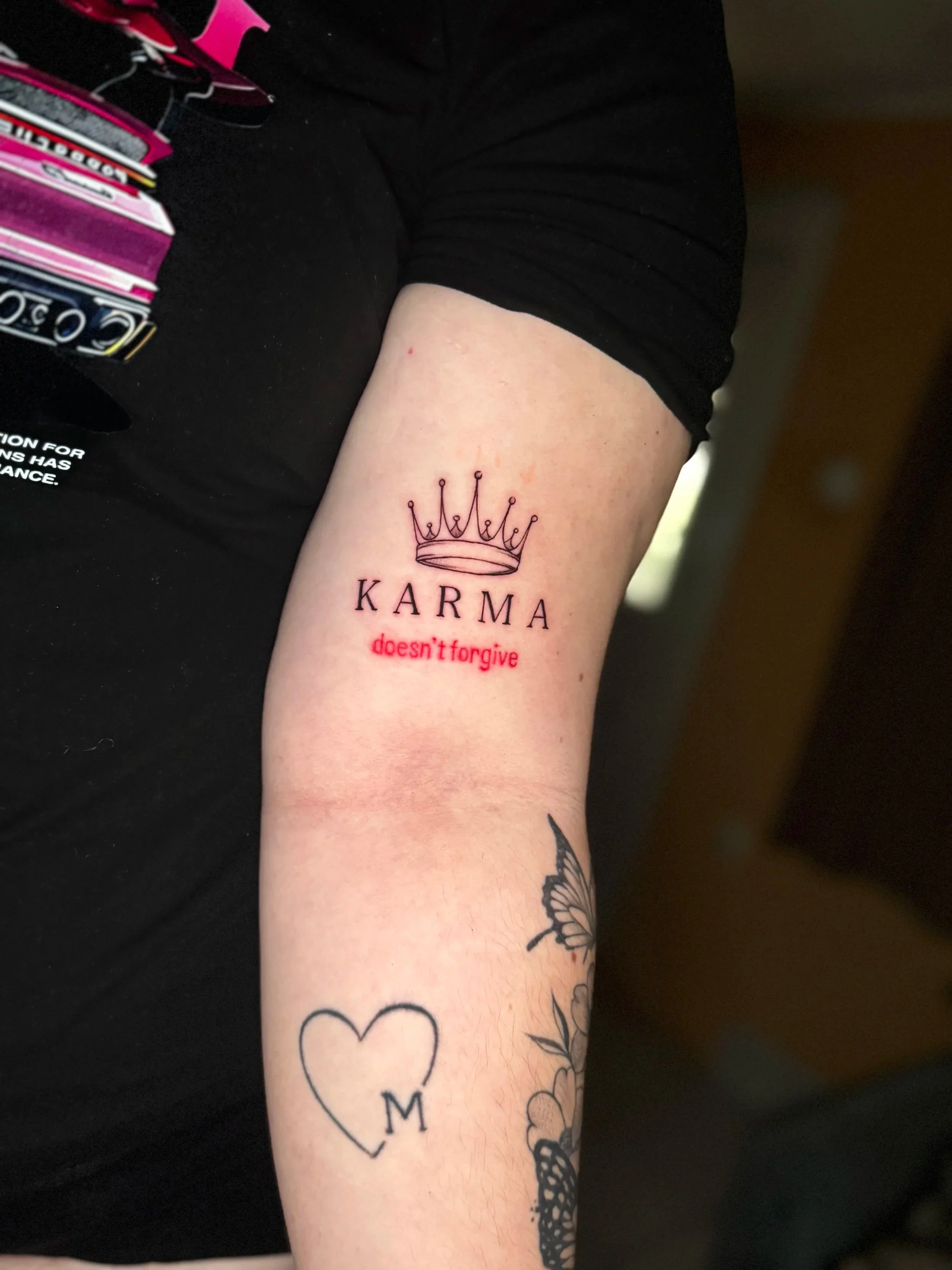 Tattoo auf dem Unterarm einer Person mit der Aufschrift ‚KARMA doesn‘t forgive‘ und einer einfachen Krone im oberen Bereich.