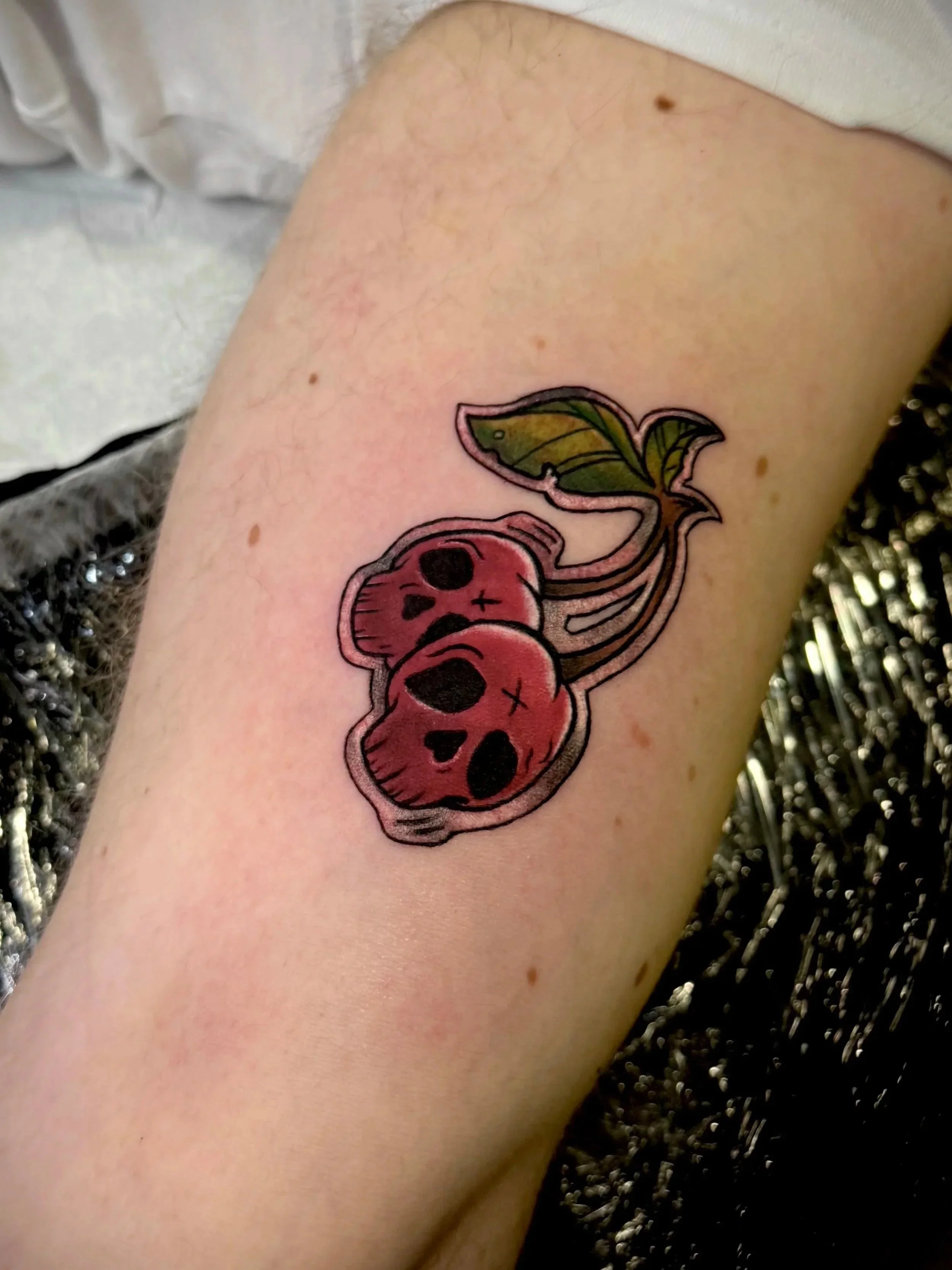 Tattoo eines Herzens mit Flügeln auf einem Oberarm, in Schwarz, mit grünen und roten Farben.