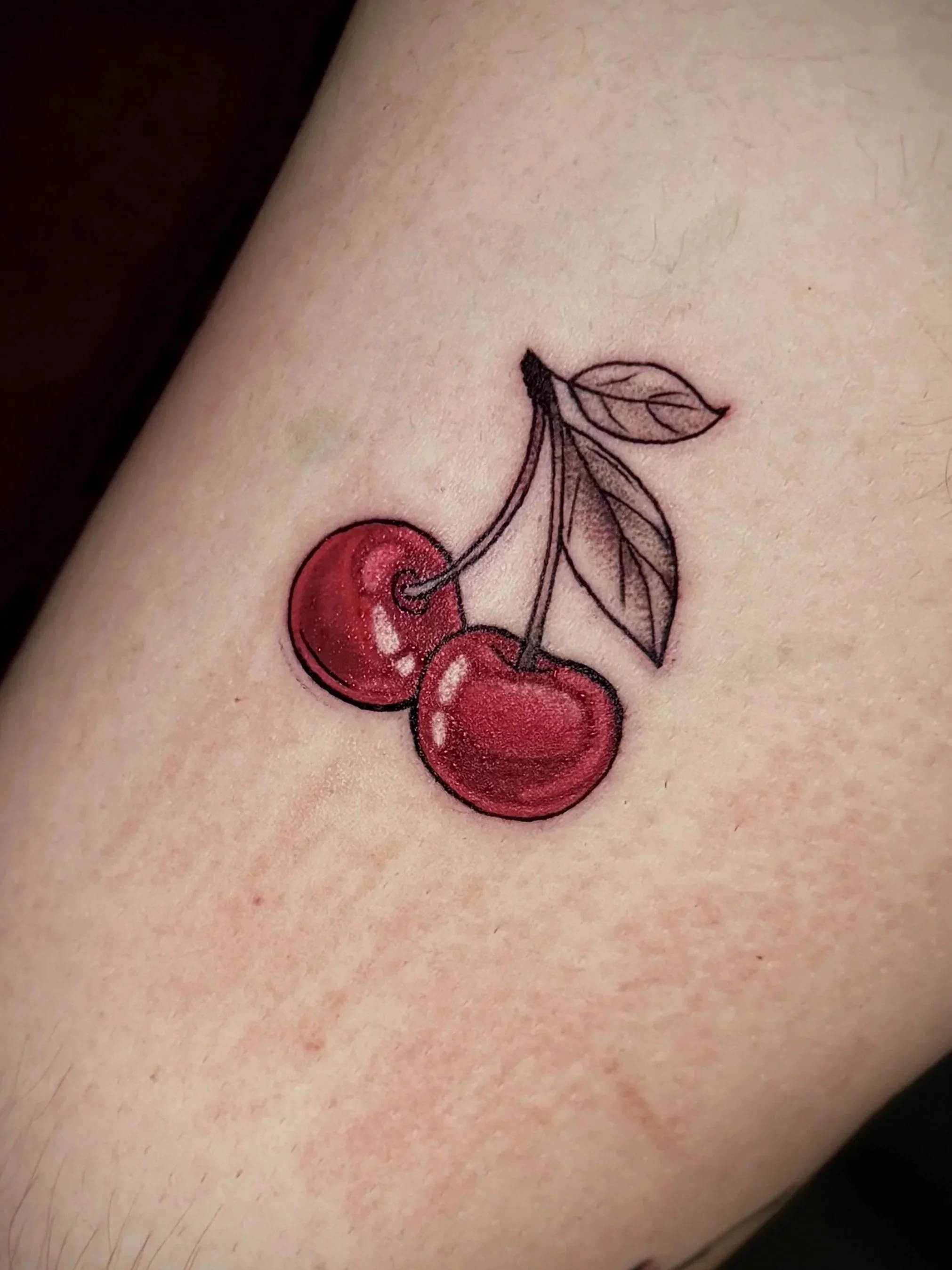 Tattoo einer Kirsche mit Blättern auf der Haut.