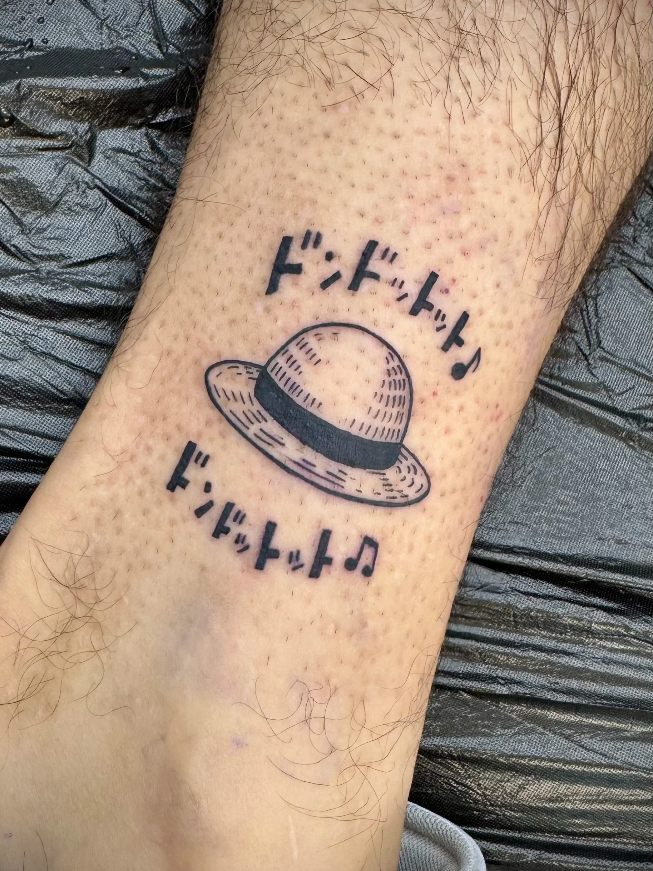 Tattoo auf einem menschlichen Bein, das einem Cowboy-Hut ähnelt, mit japanischen Schriftzeichen darüber.