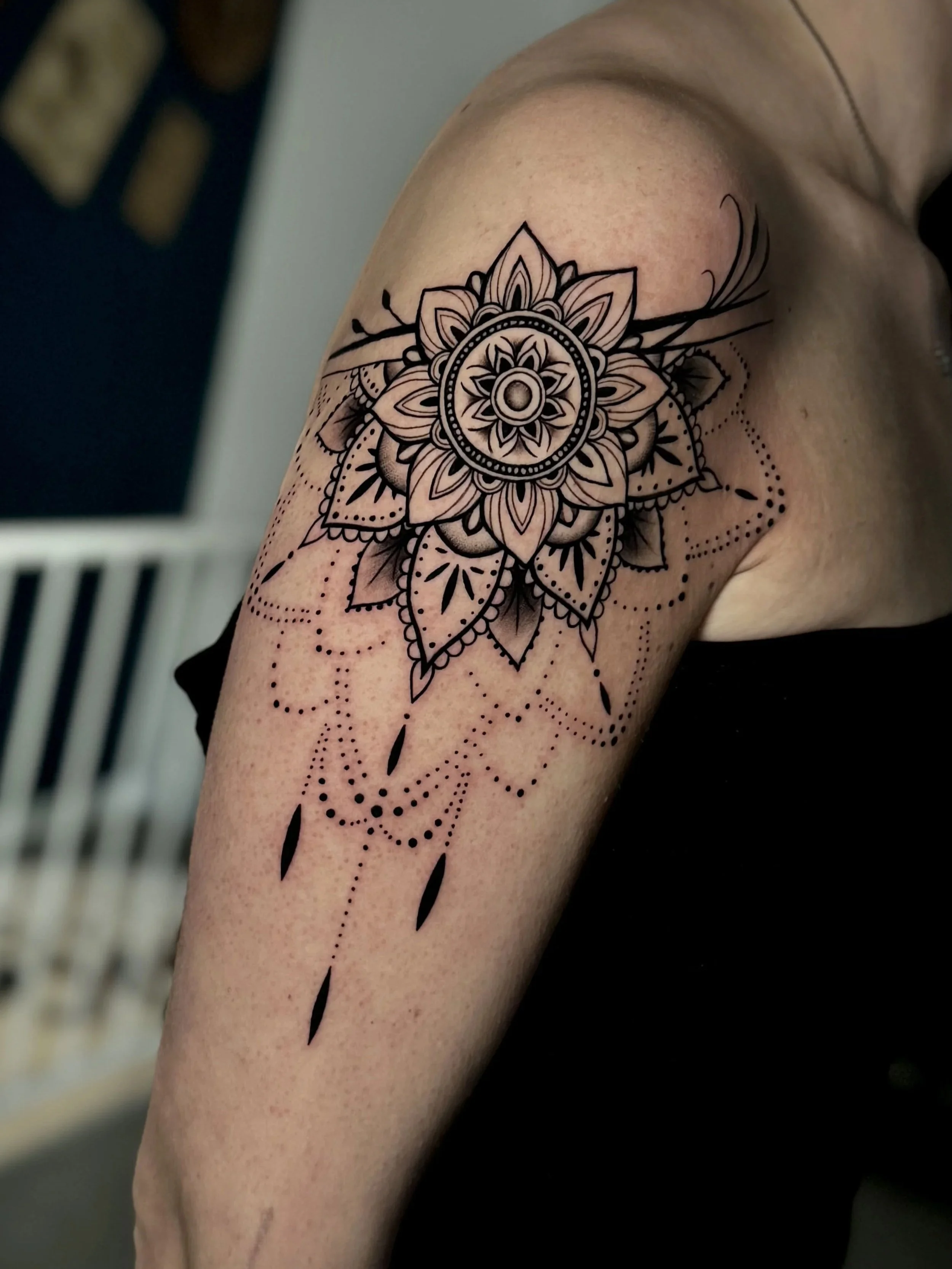 Schwarz-weiße Mandala-Tätowierung auf Oberarm mit Blumenmuster, Linien und Punkten.
