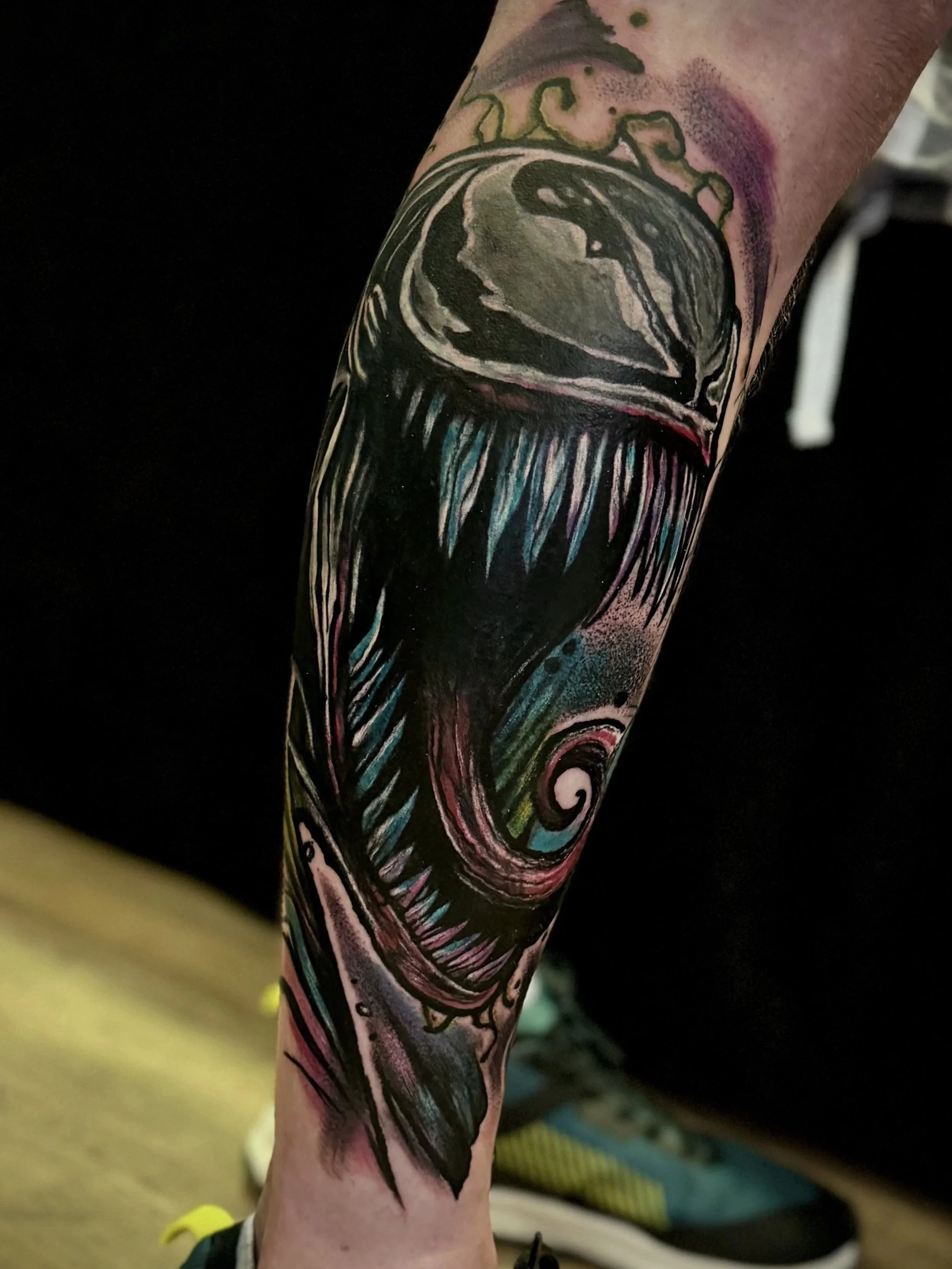 Tattoo auf dem Unterschenkel, das einen weinenden Joker mit grünen Haaren und einem lächelnden Mund zeigt, mit bunten, comic-artigen Details.