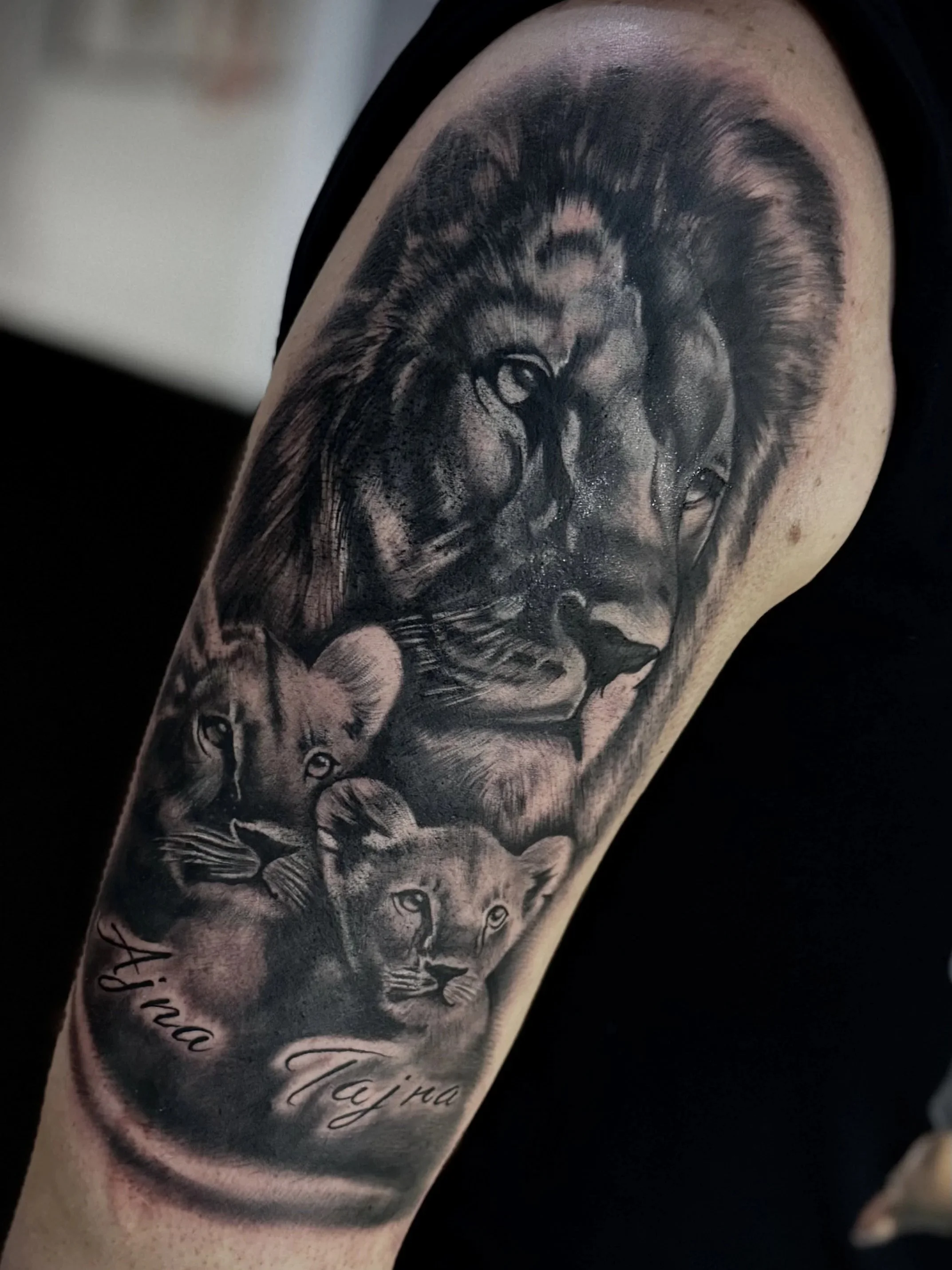 Tattoo eines Löwen und eines Leoparden auf einem Arm, in schwarz-weißer Silberiglio-Optik, mit Text darunter.