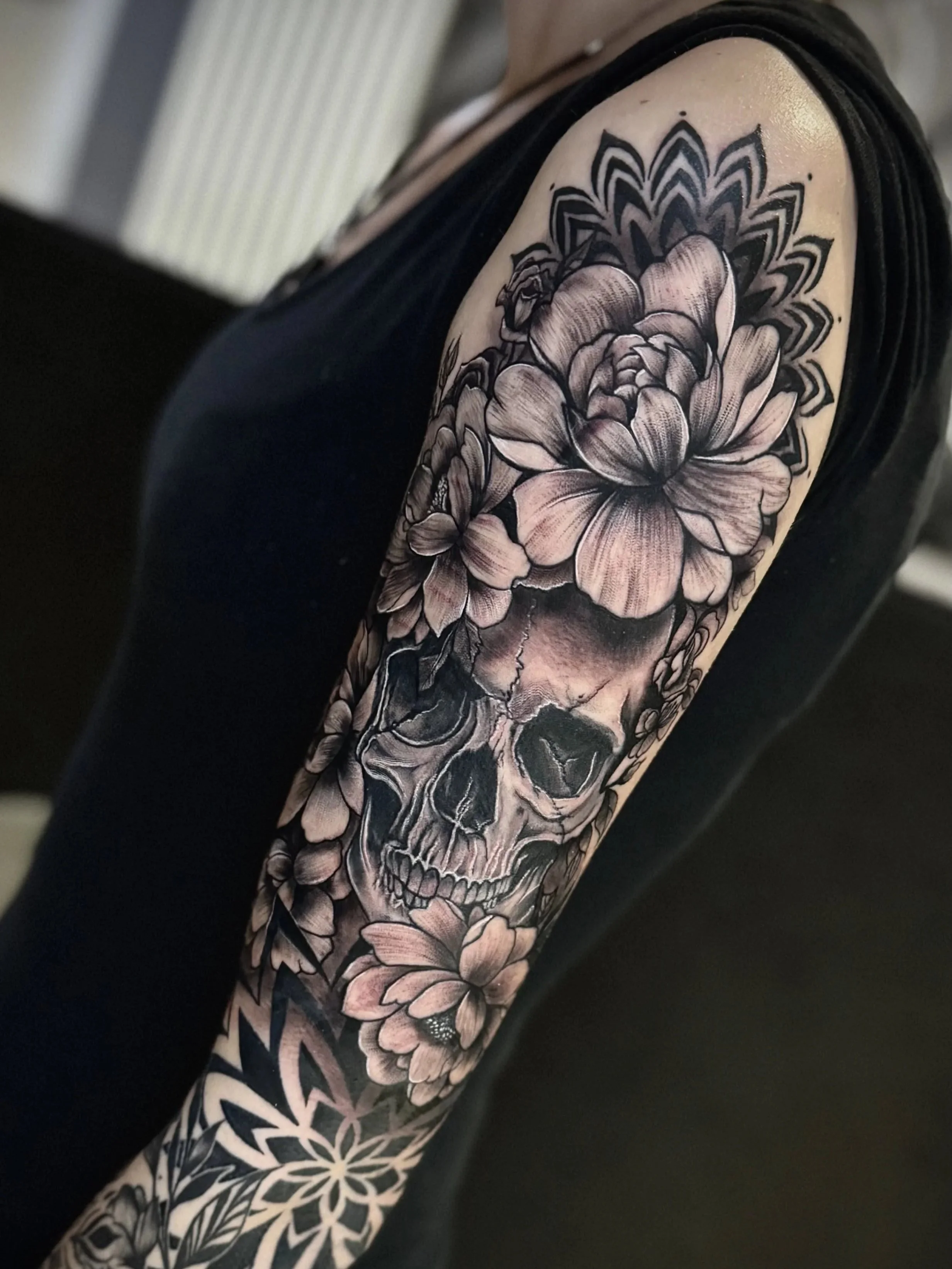 Ein Tattoo auf einem Arm, das einen Totenkopf mit Blumen und geometrischen Mustern zeigt.