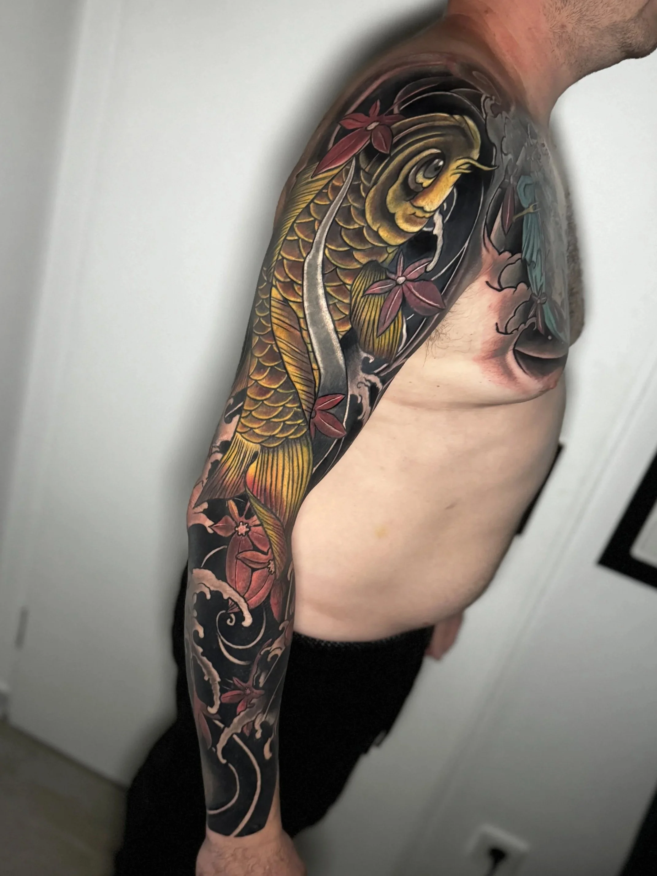 Tattoo eines Fisches auf dem Arm mit roten Blumen und Wasserwellen im japanischen Stil.