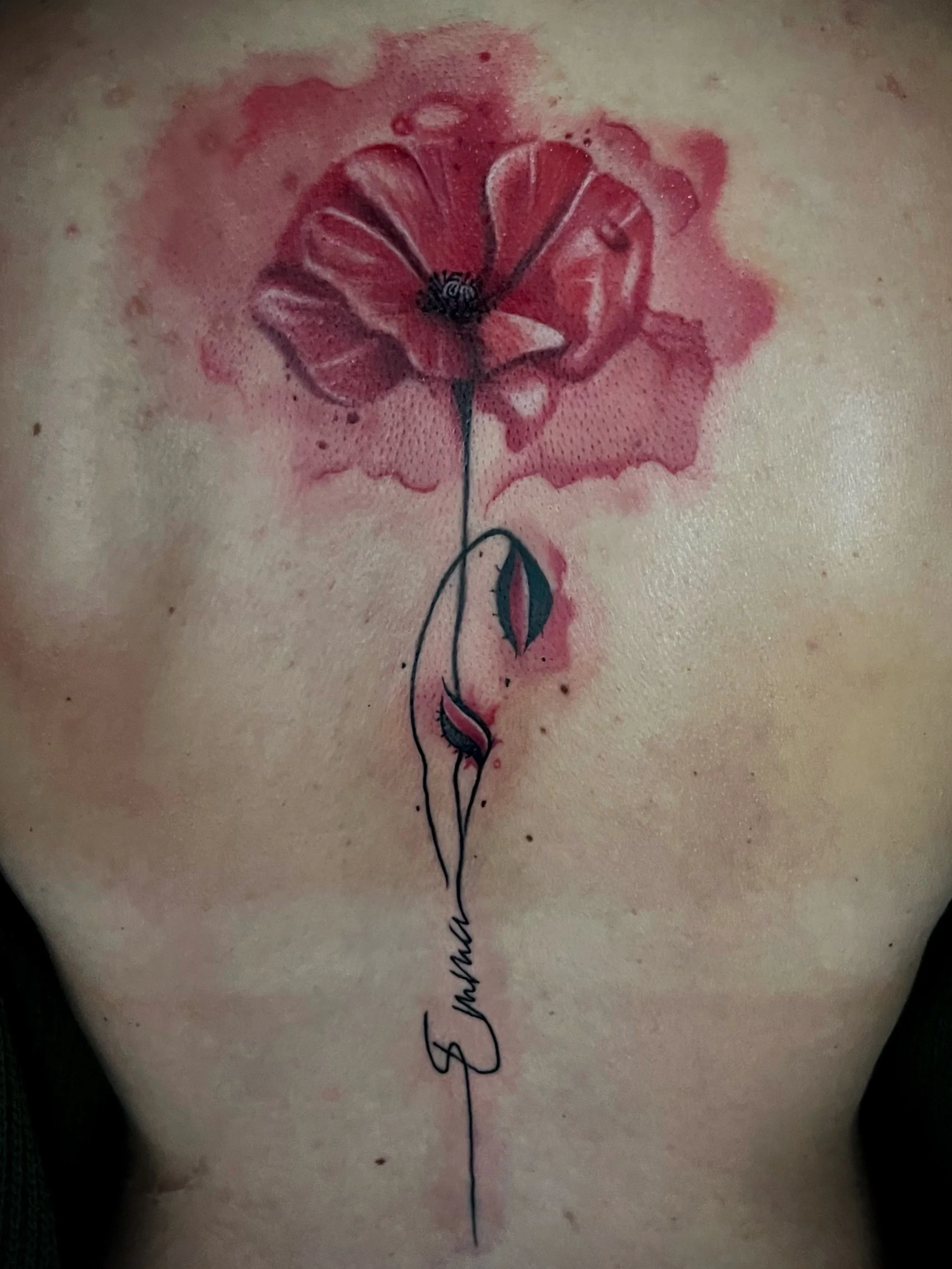 Tattoo eines roten Rosenblatts mit schwarzen Linien und einem grünen Stiel, das in eine geschwungene schwarze Schrift integriert ist.