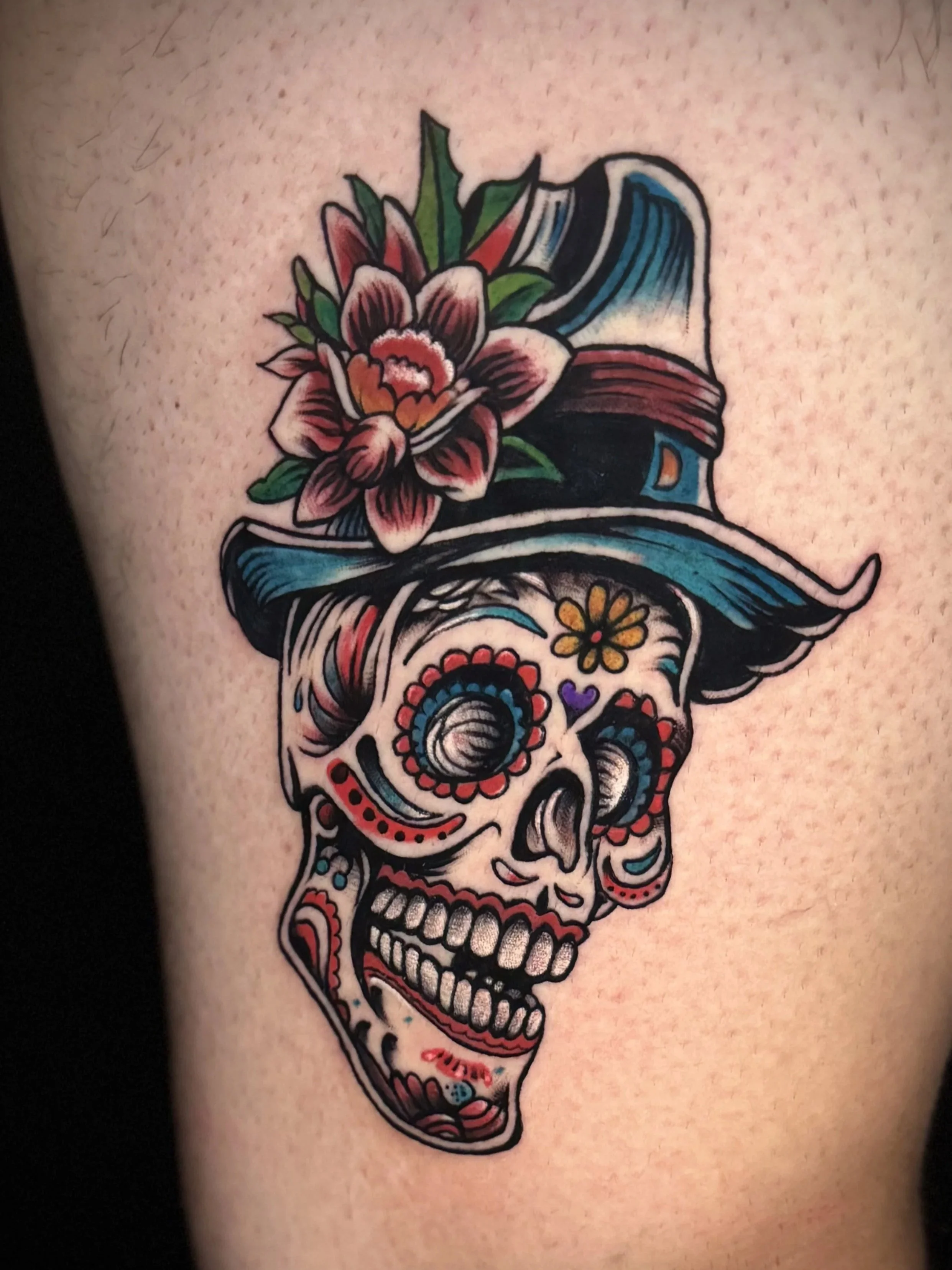 Tattoo eines bunten Totenkopfs mit Blumen und Lackmustuken-Designs auf der Haut.