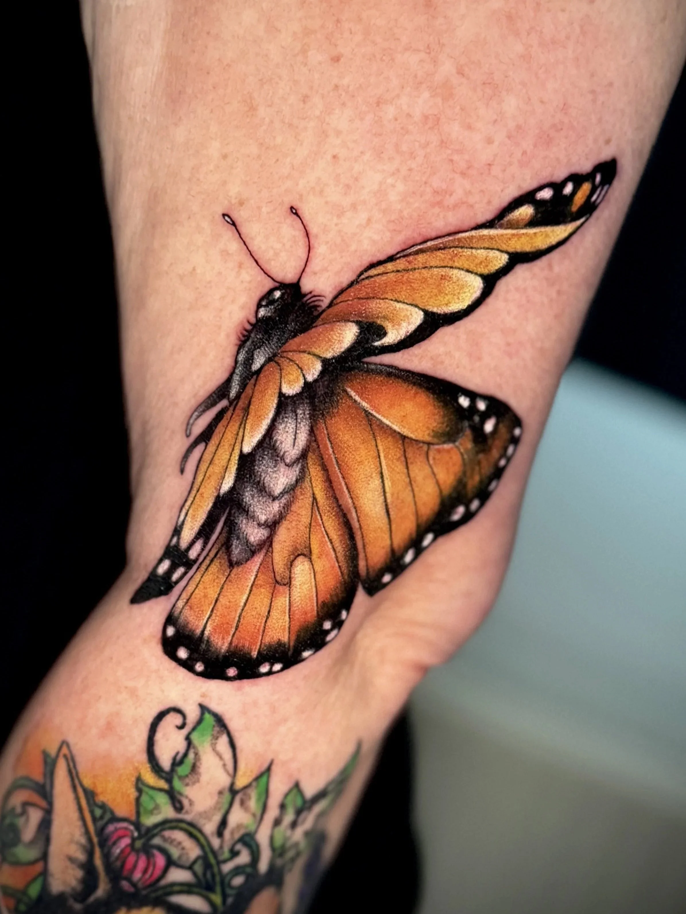 Tattoo eines Schmetterlings auf dem Arm, hauptsächlich in orange, schwarz und weiß gehalten.
