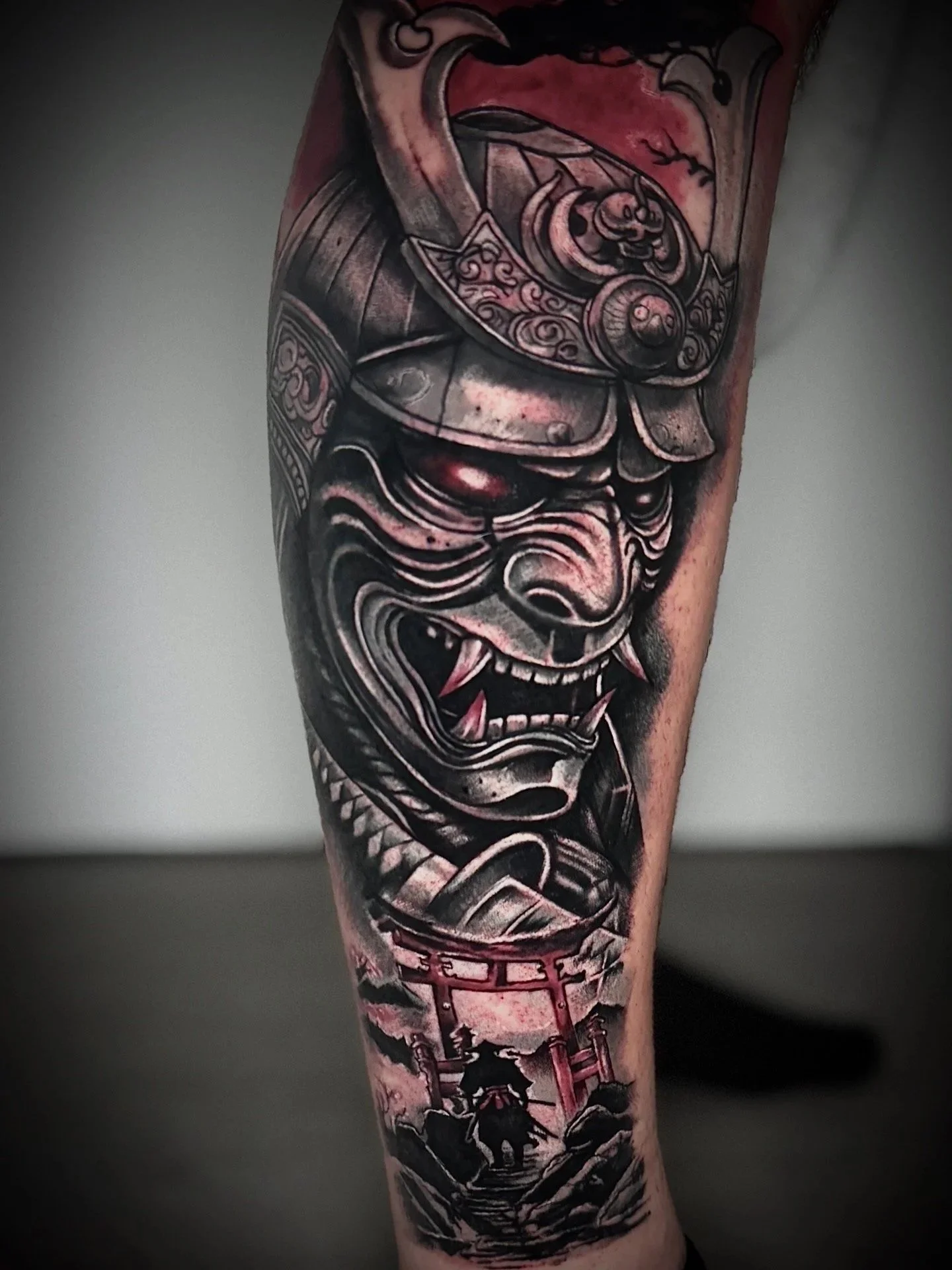 Tattoo eines japanischen Oni-Gesichts in Schwarz und Rot auf dem Arm, mit traditionellen Elementen