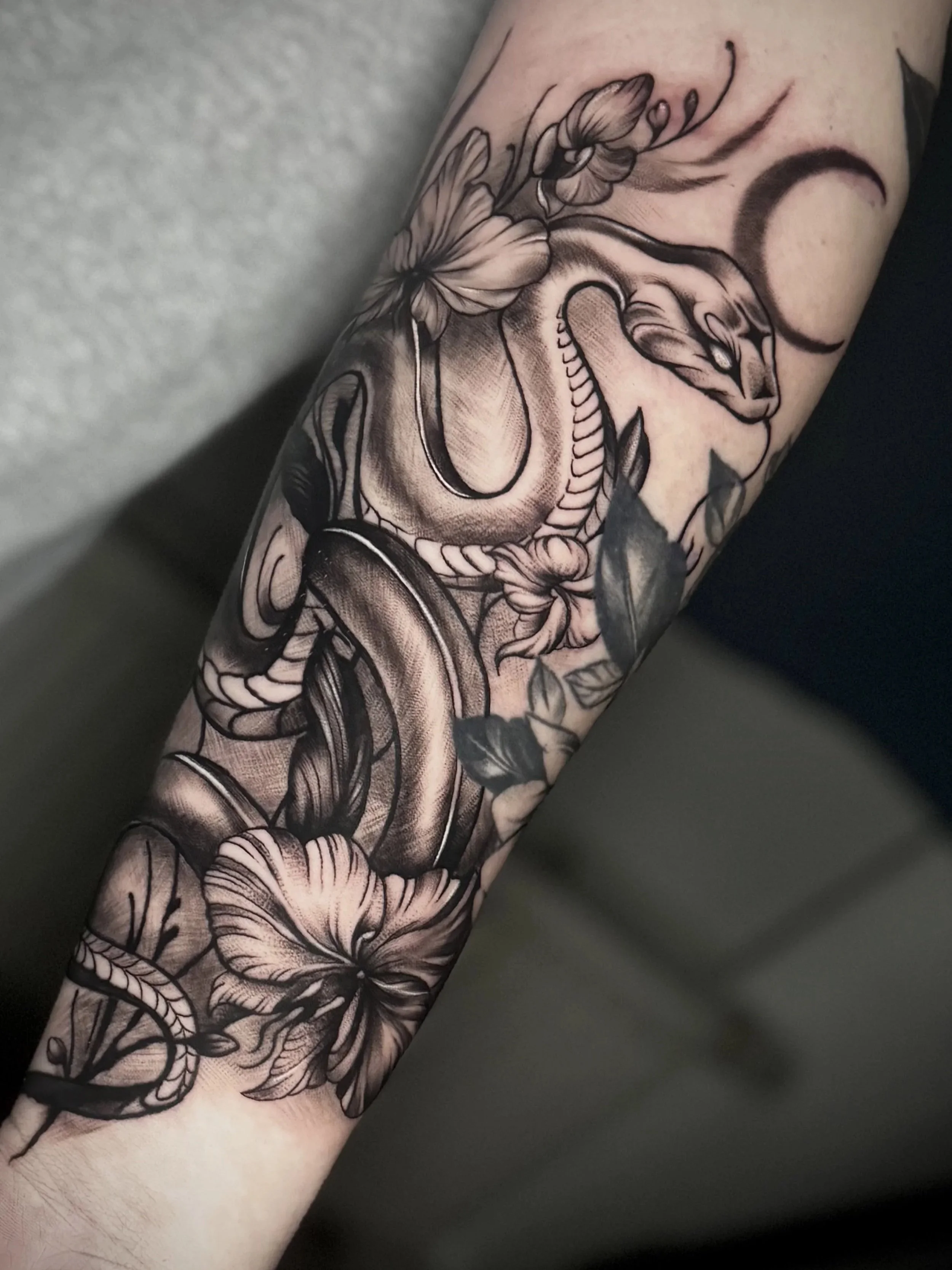 Schwarze und graue Tattoo eines Schlangen- und Blumenmusters auf einem Unterarm.