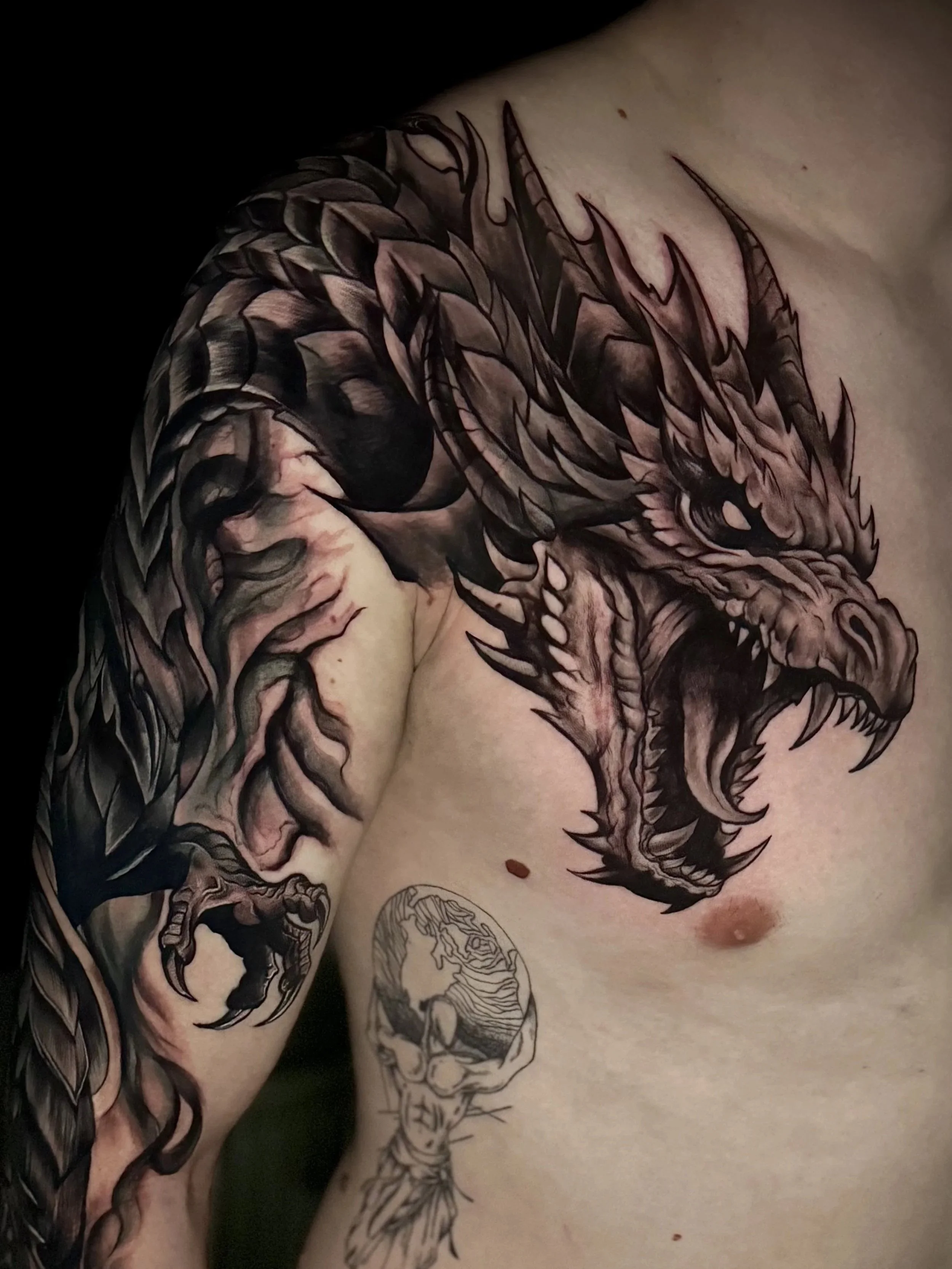 Tattoo eines feuerspeienden Drachen auf der Schulter und Arm eines Menschen.