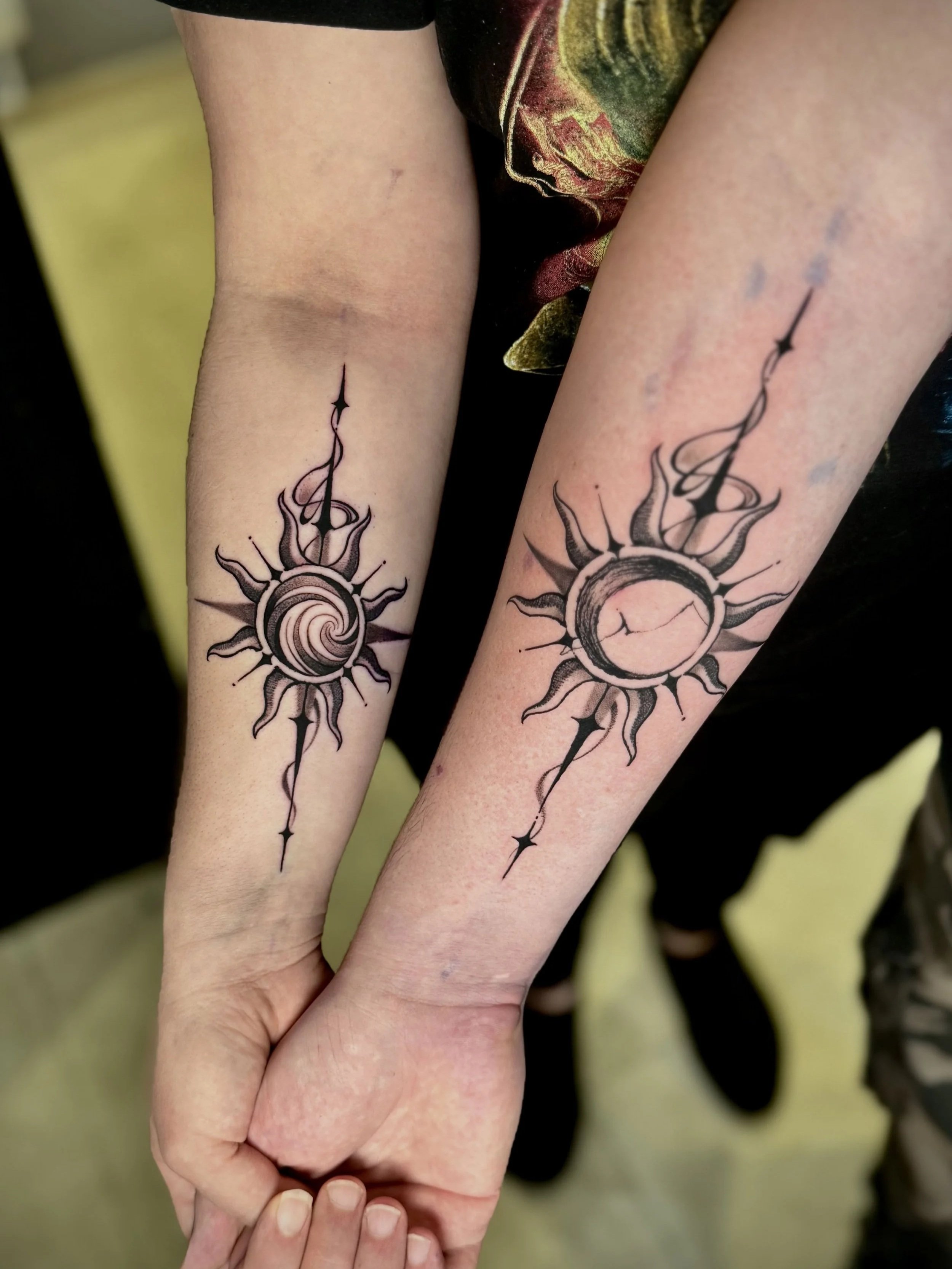 Zwei Arme mit schwarzen Sonnen-Tattoo, die sich gegenseitig halten