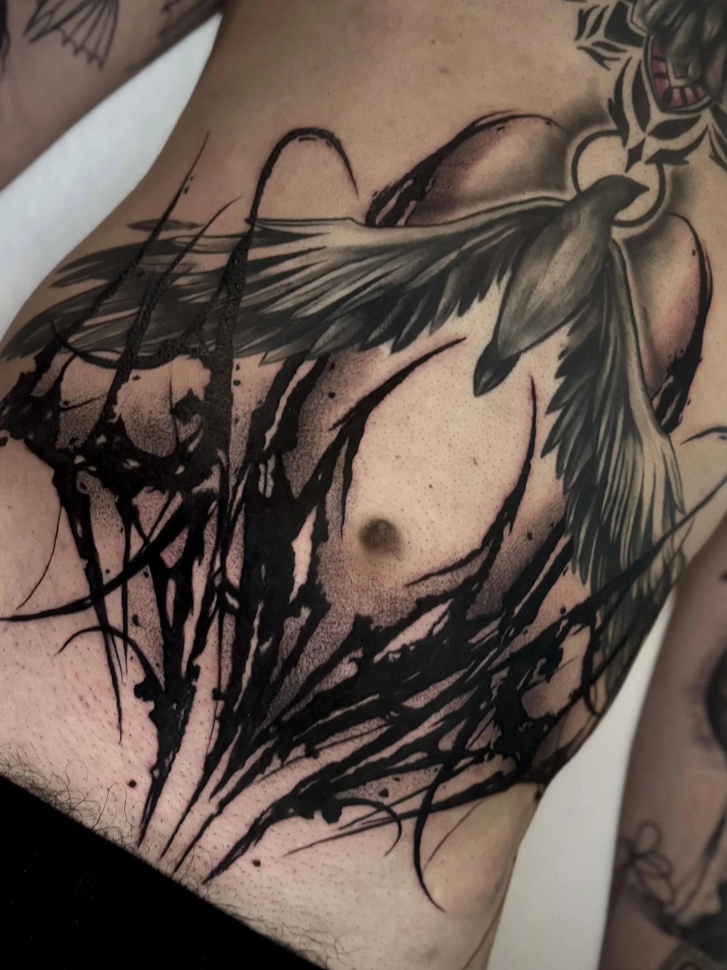 Tattoo eines Vogels mit Flügeln auf der Brust, umgeben von schwarzen Linien und dunklen Akzenten.