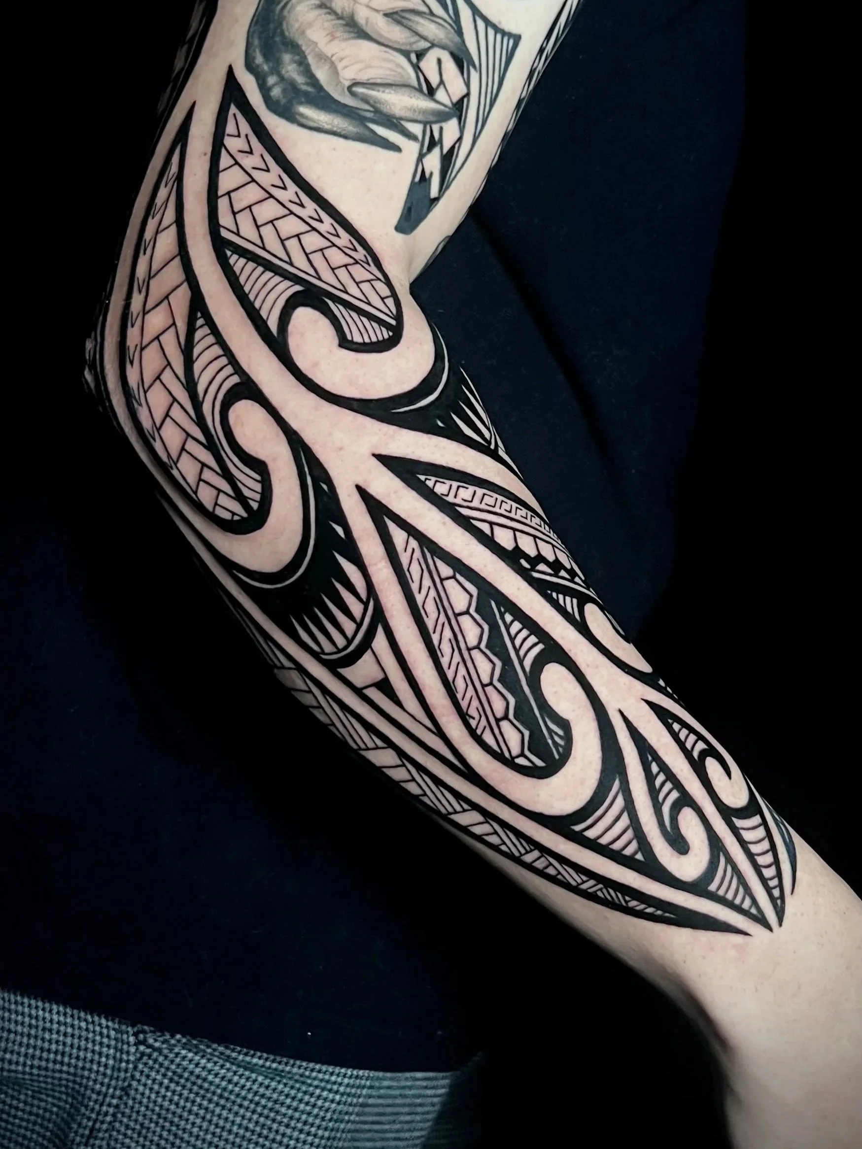 Ein Tattoo mit schwarzen Linien und geometrischen Mustern auf einem oberen Arm, mit Details in Schwarz und Grau.