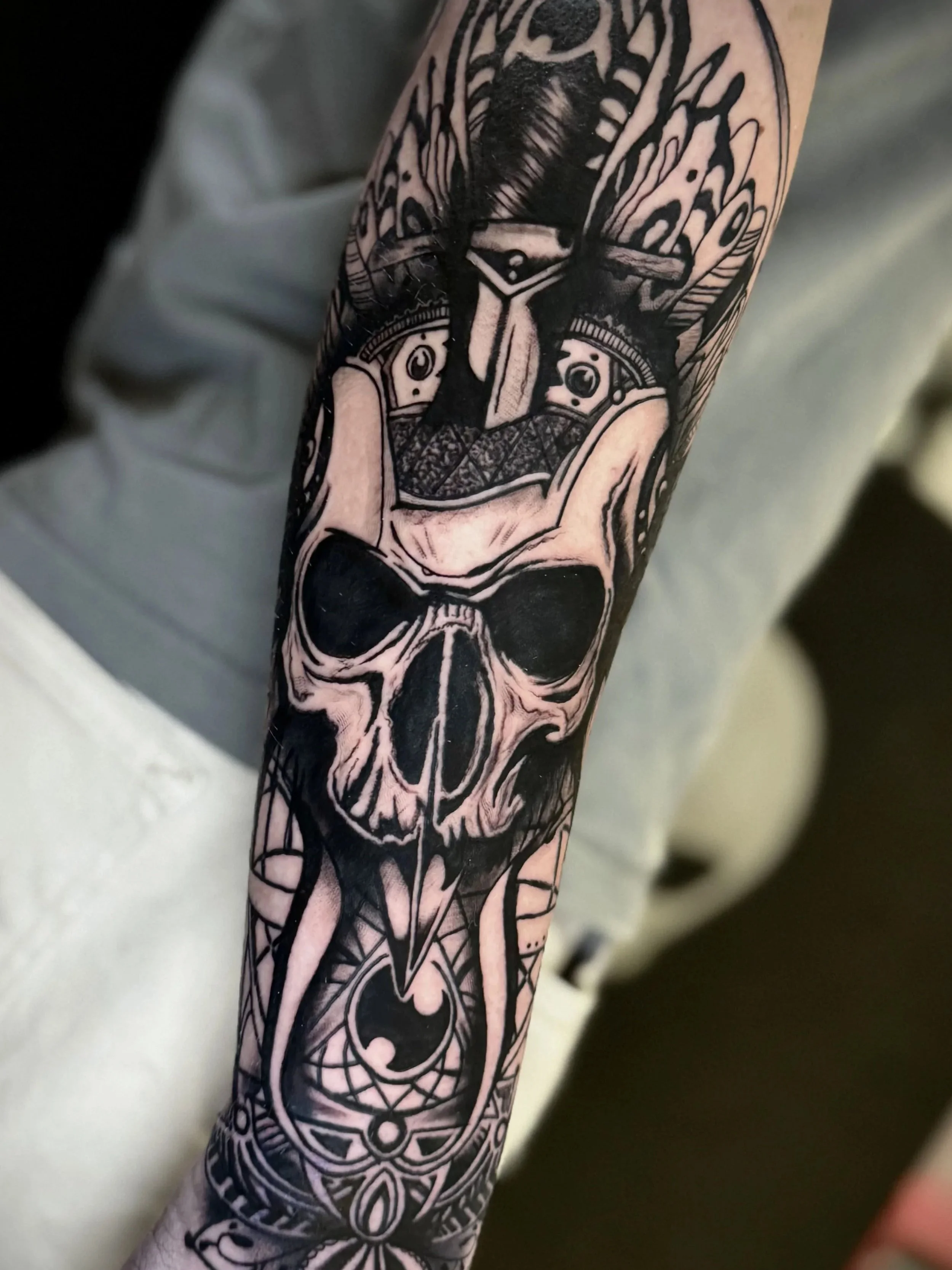 Schwarzes Tattoo am Unterarm mit geometrischem und symbolischem Design, einschließlich eines Schädels, Kreisen und Linien.