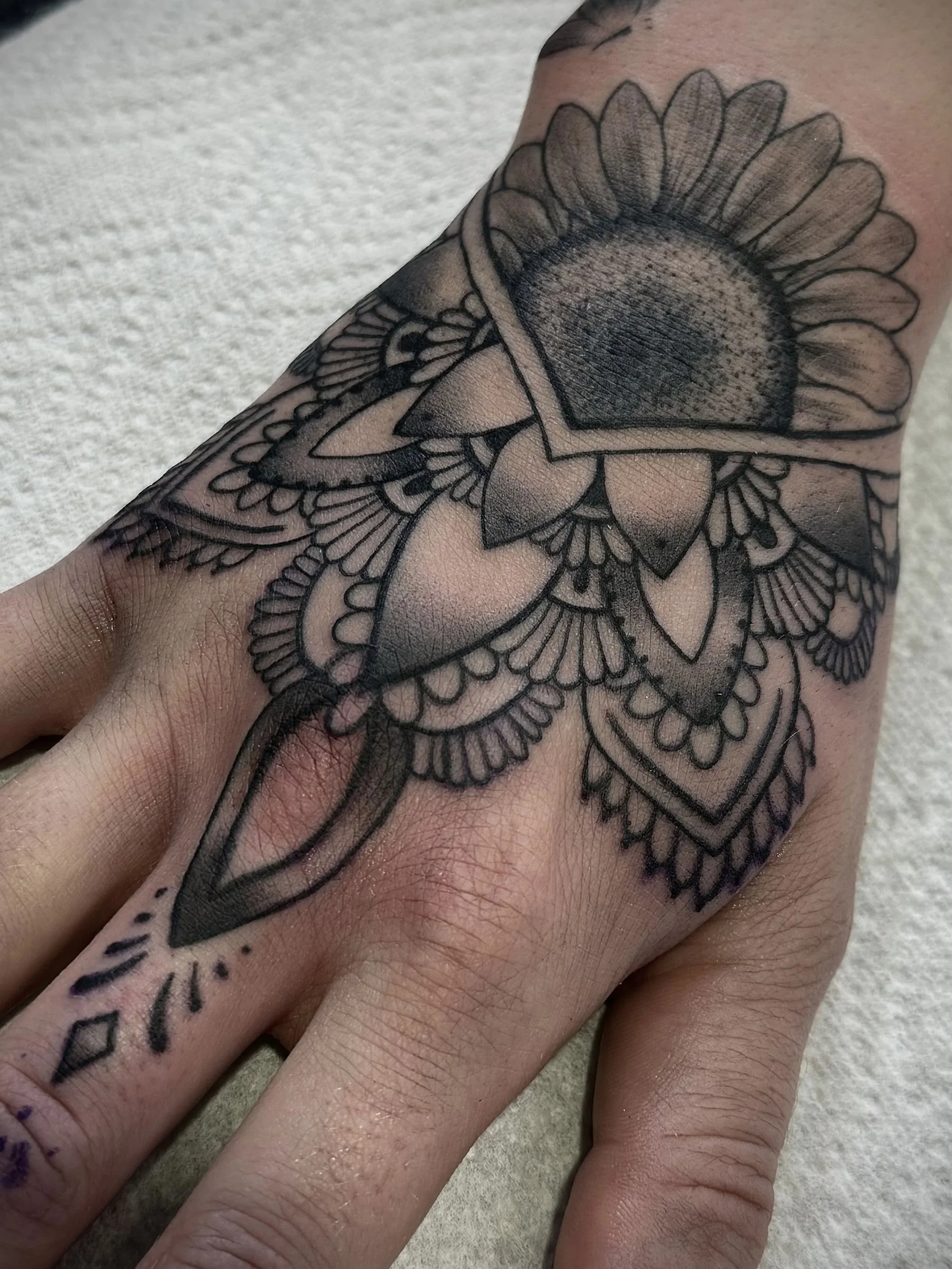 Tattoo einer Sonnenblume auf der Hand mit schwarzen Linien und Schattierungen.