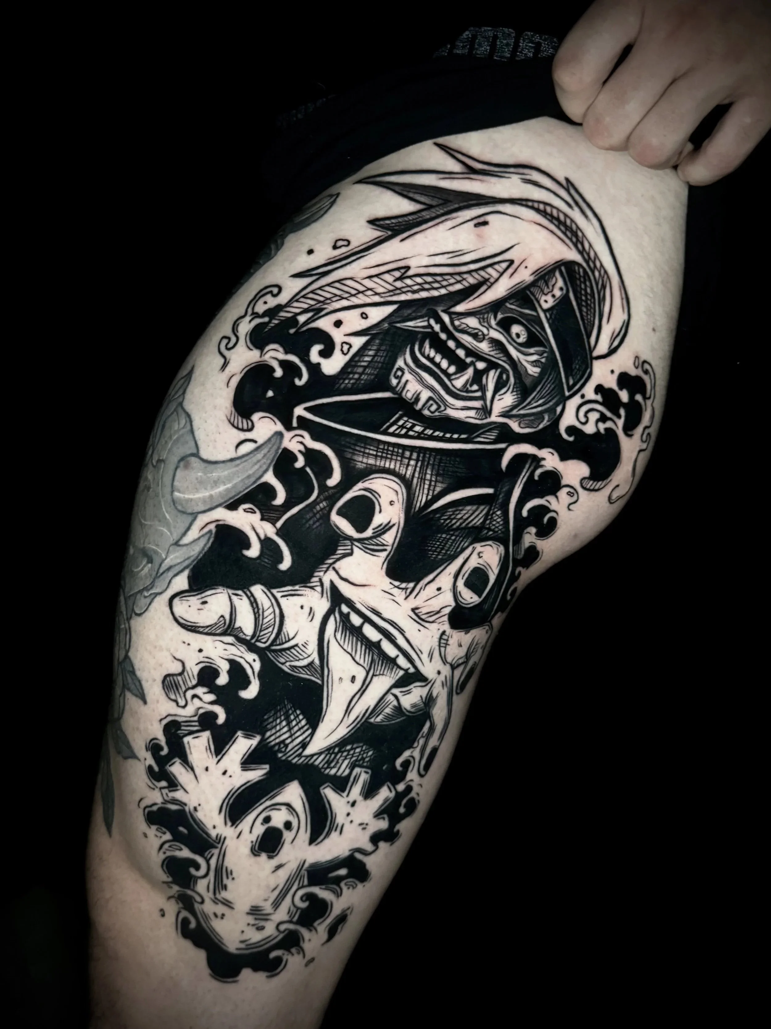 Schwarzes Tattoo auf dem Arm eines Menschen, das einen gehirnähnlichen Schädel mit Flammen und Wellenmuster zeigt.