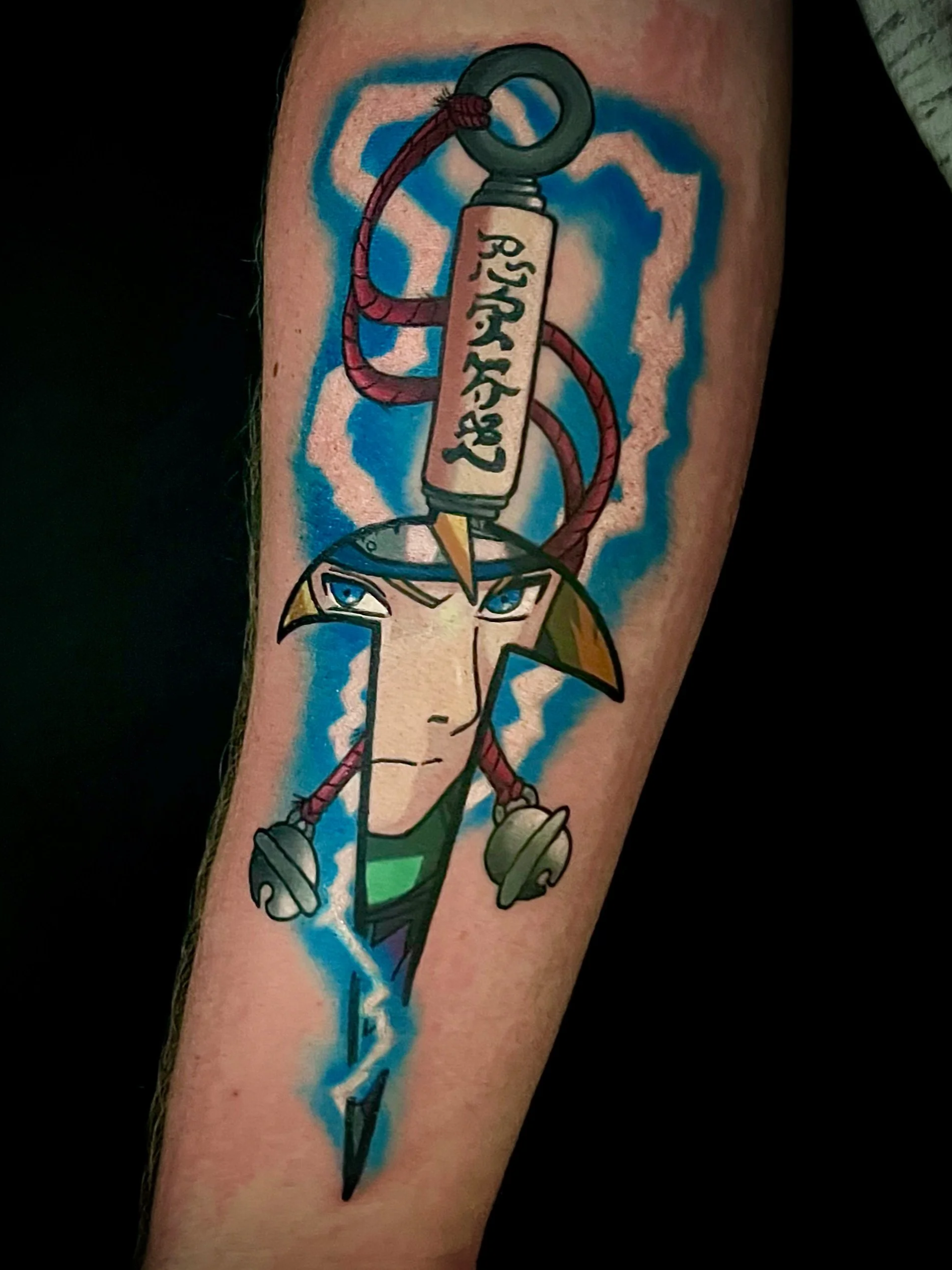 Tattoo auf dem Oberarm eines Menschen, zeigt eine cartoonartige Einhornfigur mit blauen Augen und rosa Mähne, gehalten von einem Schraubenschlüssel. Im Hintergrund sind blaue und orangene Farben, umgeben von einem blau-weißen Blitzeffekt.