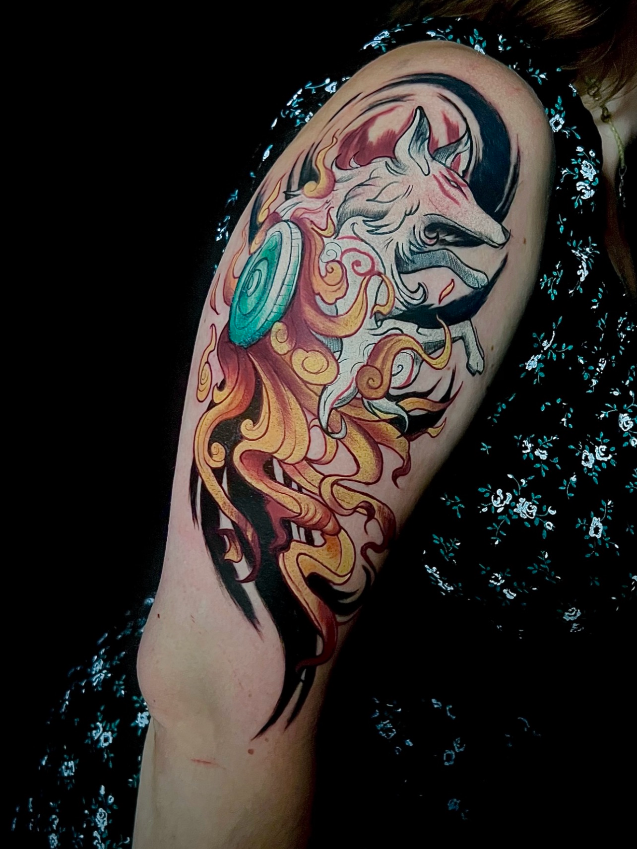 Tattoo eines Einhorns auf dem Oberarm mit bunten Flammenmotiven im Stil des japanischen traditionellen Tattoos, mit schwarzem Hintergrund.