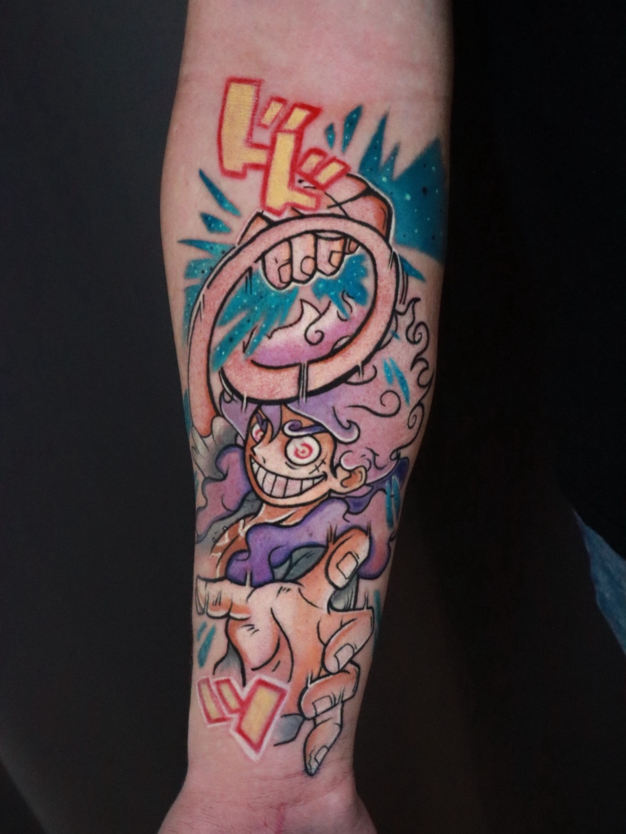 Tattoo eines Comic-Charakters mit grinsendem Gesicht, spiralförmigen Augen, einer Hand mit ausgestrecktem Zeigefinger, umgeben von blauen, pinkfarbenen und gelben Akzenten.