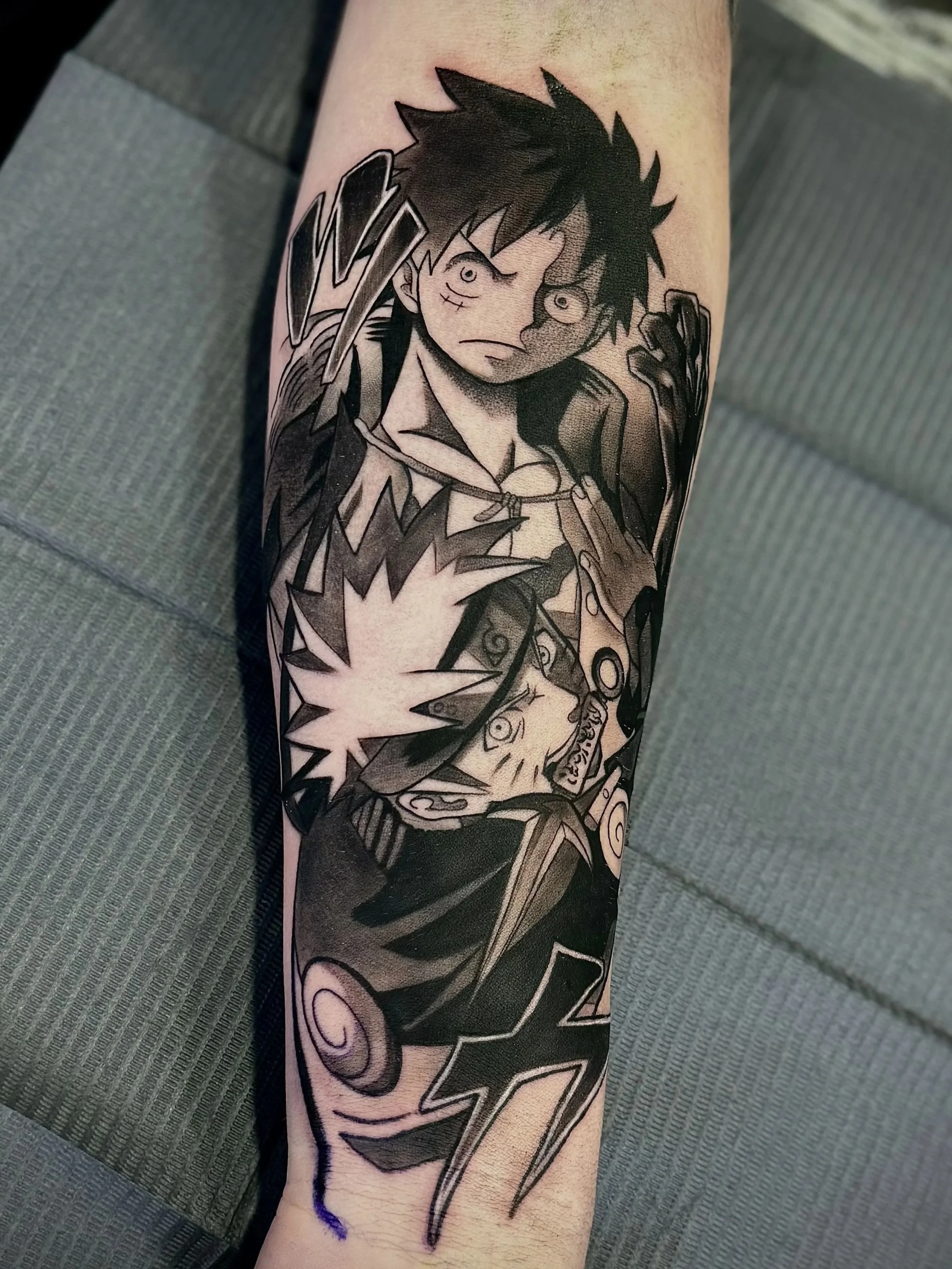 Schwarz-weiße Tätowierung eines Anime-Charakters mit wilden Haaren, großer Waffe und traditionellem Outfit auf einem Unterarm.