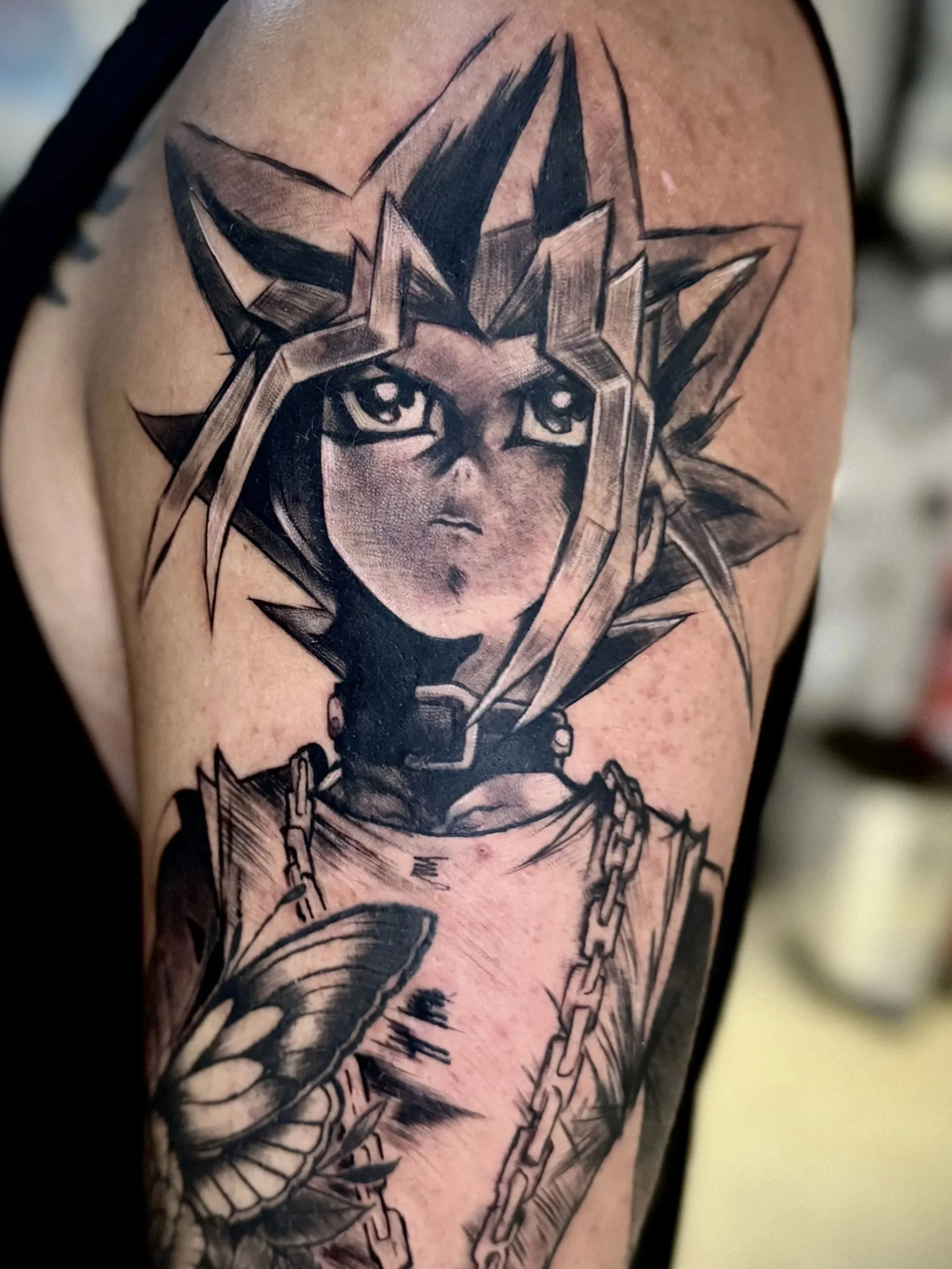 Schwarze Tätowierung eines stilisierten Gesichts einer Frau mit markanten Augen, umgeben von geometrischen Elementen und Ketten, auf einem menschlichen Arm.