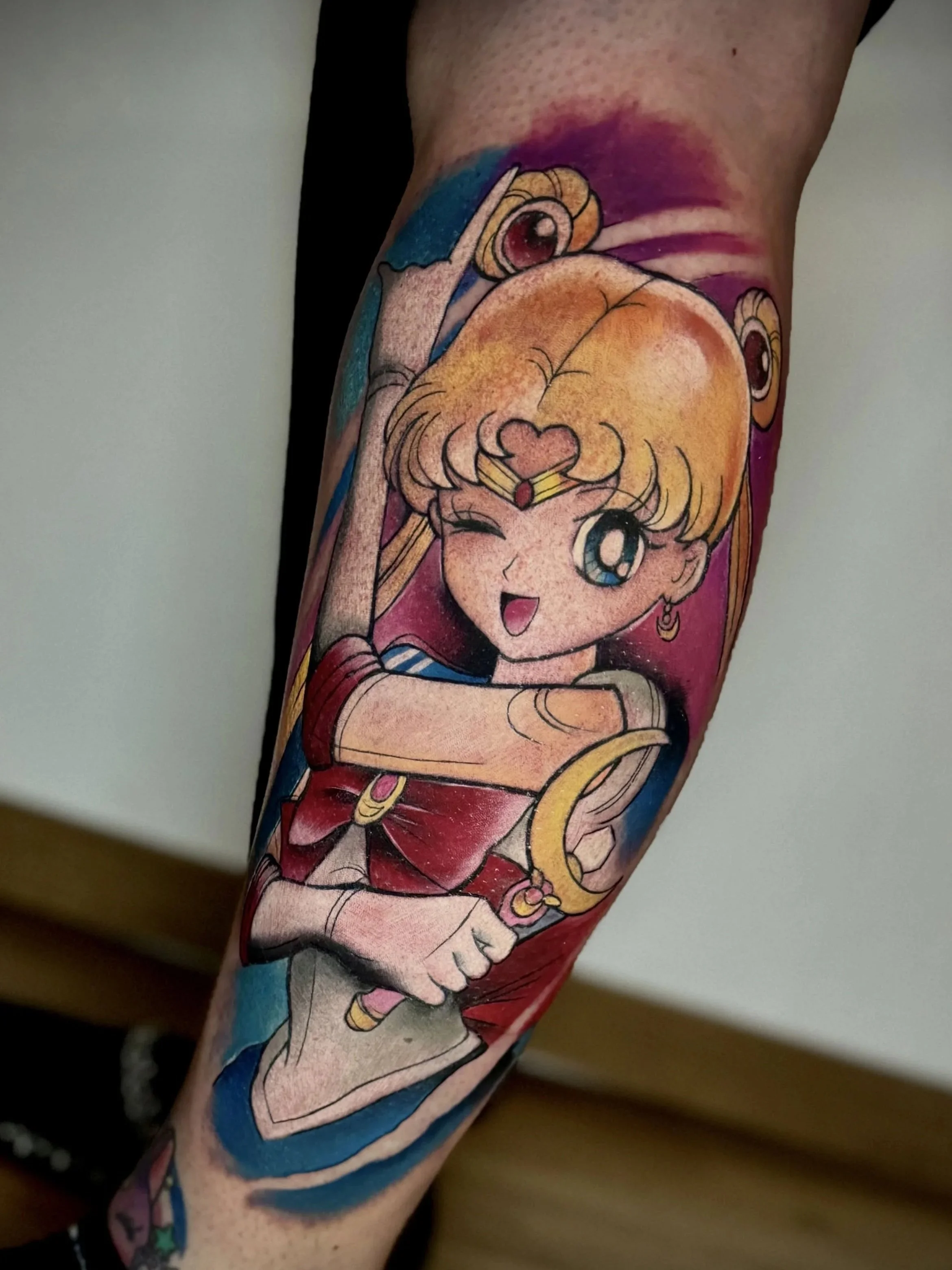 Ein farbenfrohes Tattoo auf einem Arm, das eine Anime-Figur zeigt, die winkt und lächelt, mit einem großen Stern und anderen dekorativen Elementen im Hintergrund.