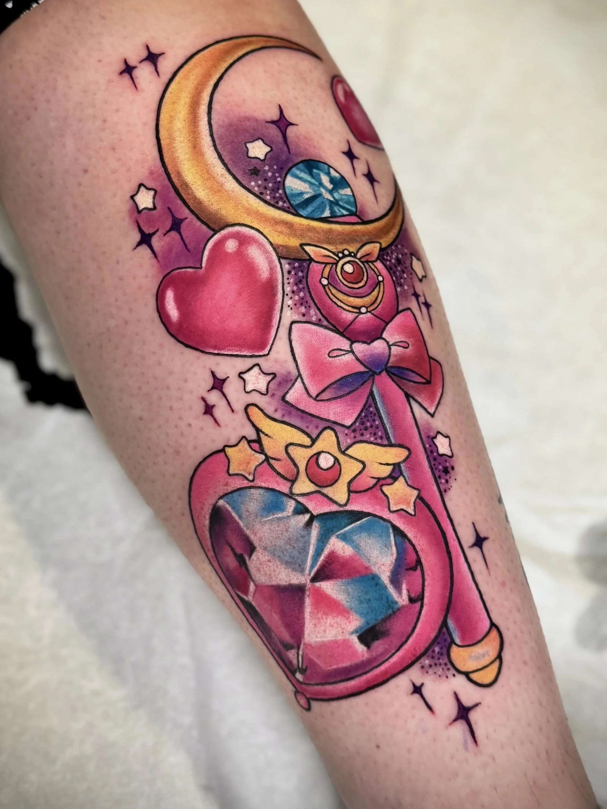 Tattoo mit rosa Herz, Mond, Sternen, Diamanten, Sternzeichen-Kreislauf und bunten Akzenten auf dem Arm.