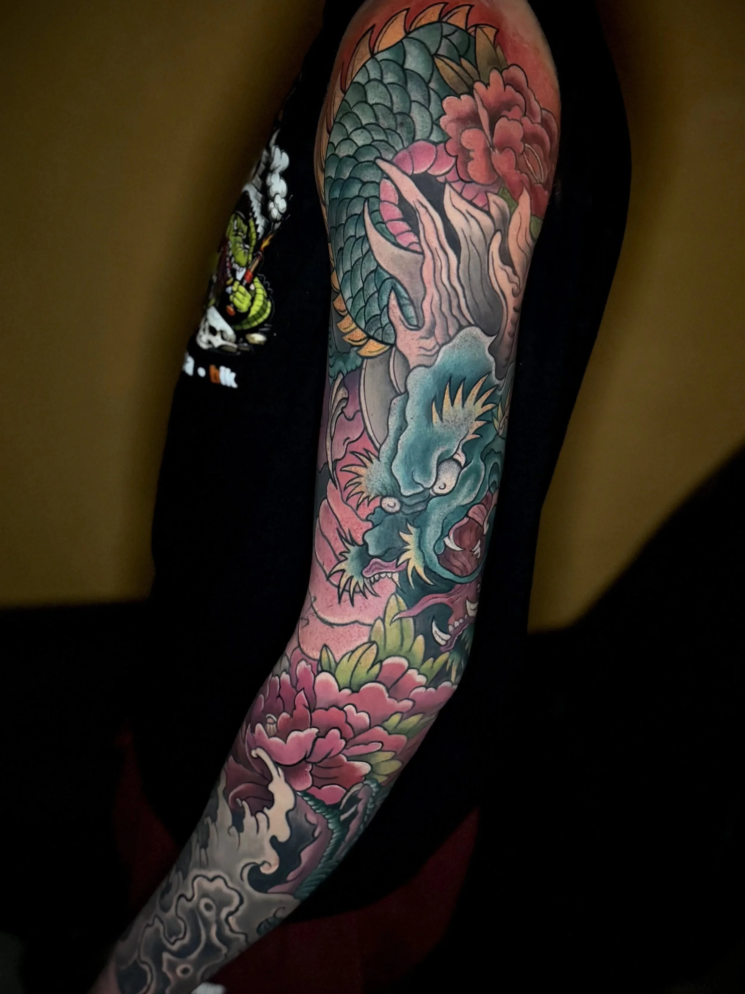 Ein Arm mit traditionellem japanischem Tattoo eines Drachen, umgeben von Blumen und Wasserwellen in leuchtenden Farben.