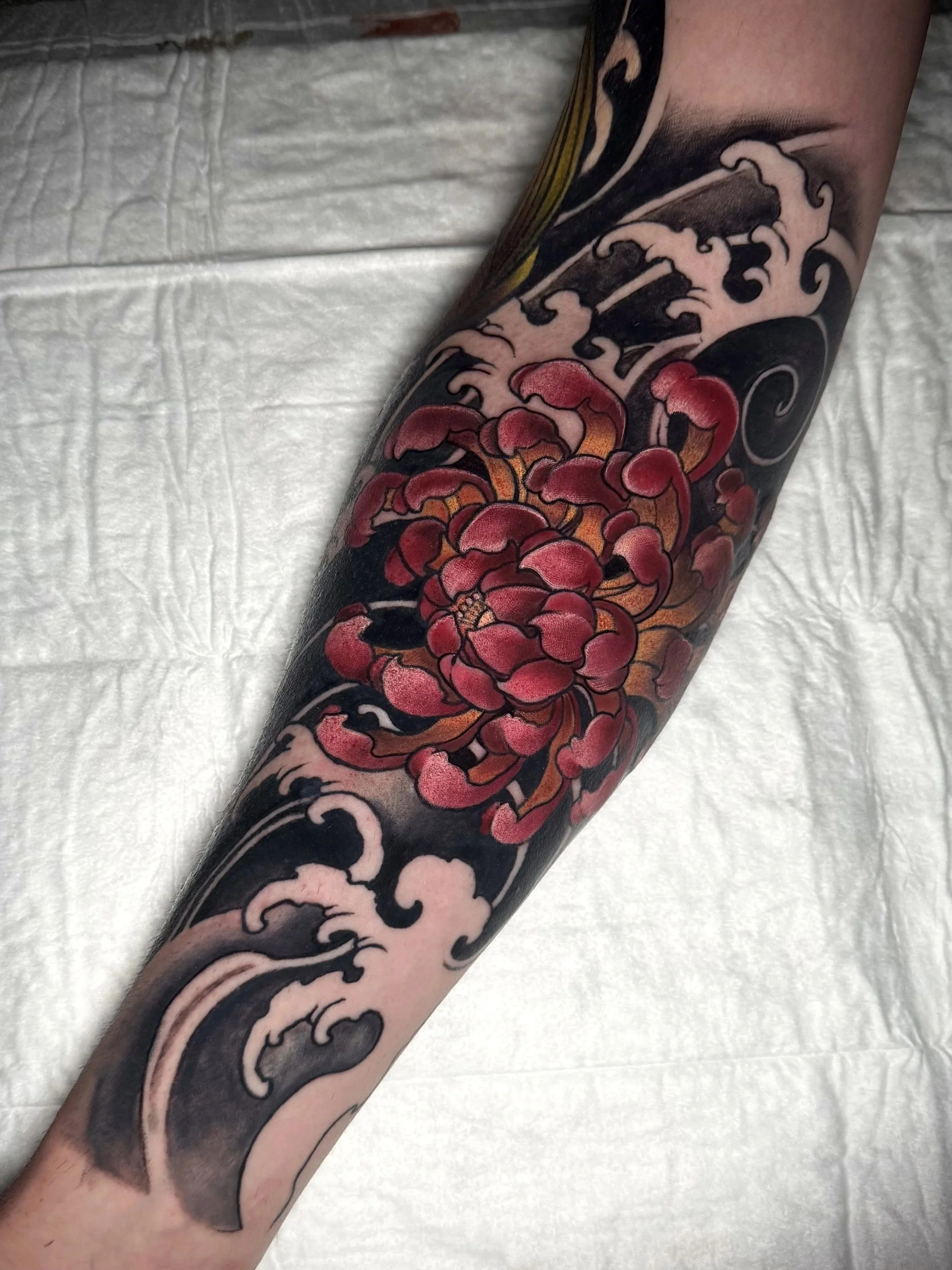 Ein Arm mit einem Tattoo, das Wellen und eine große rote Blume zeigt.